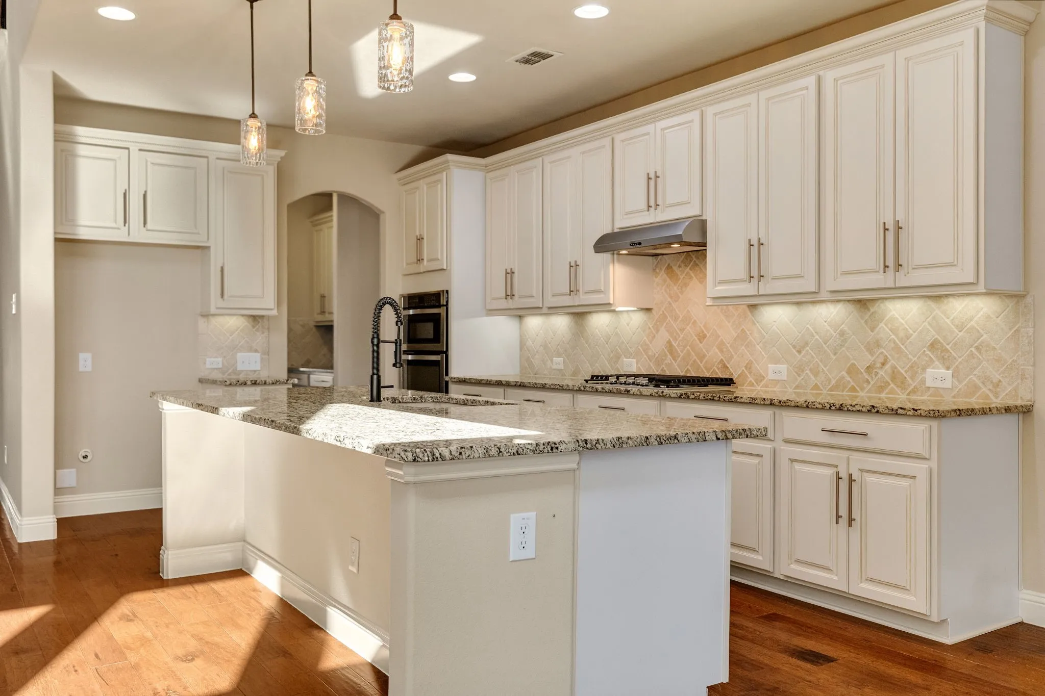Spacious kitchen featuring an island with breakfast area, light-toned cabinetry, herringbone tile backsplash, and wood-finish flooring