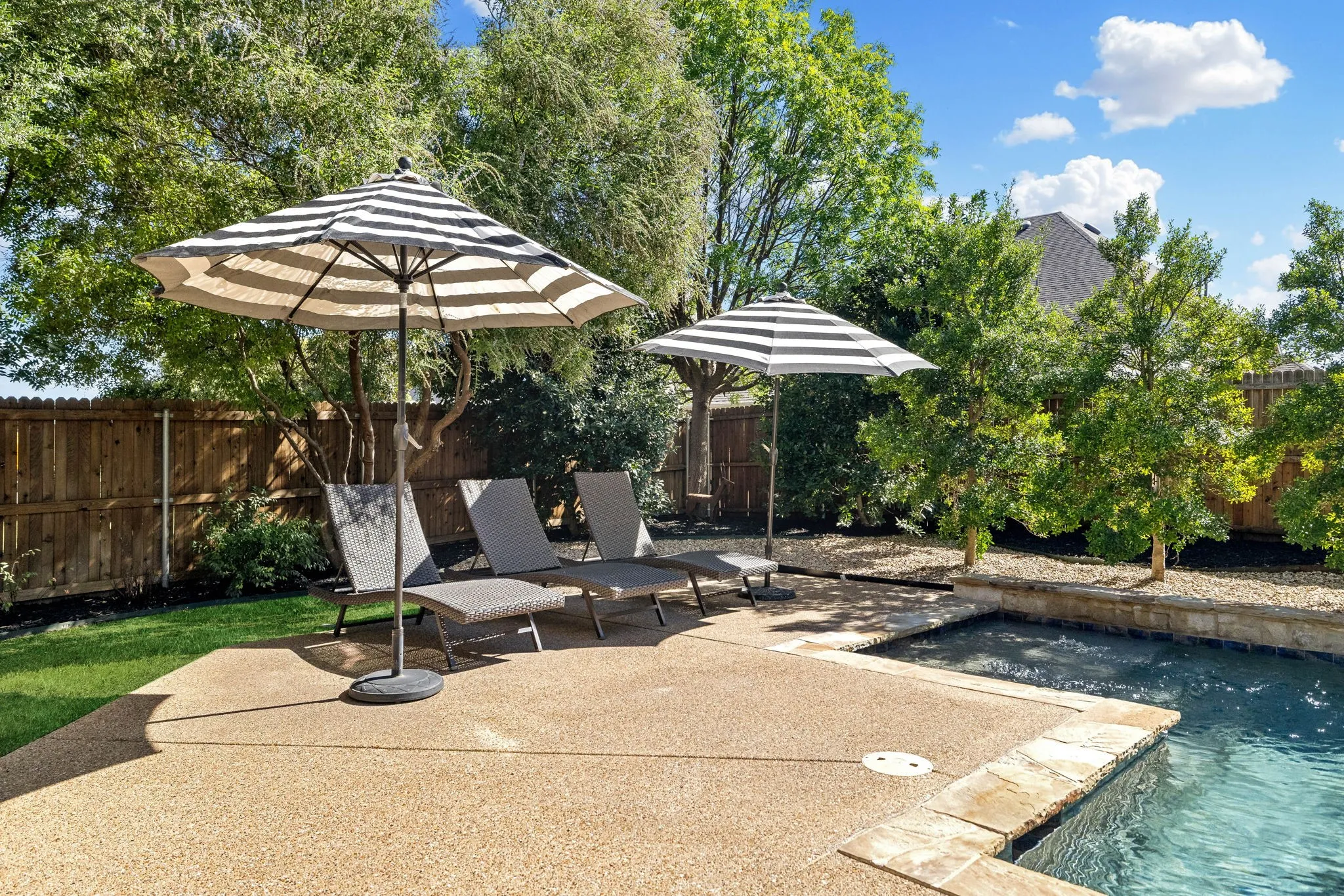 Outdoor space featuring a swimming pool, stone coping, aggregate concrete decking, and a wood privacy fence