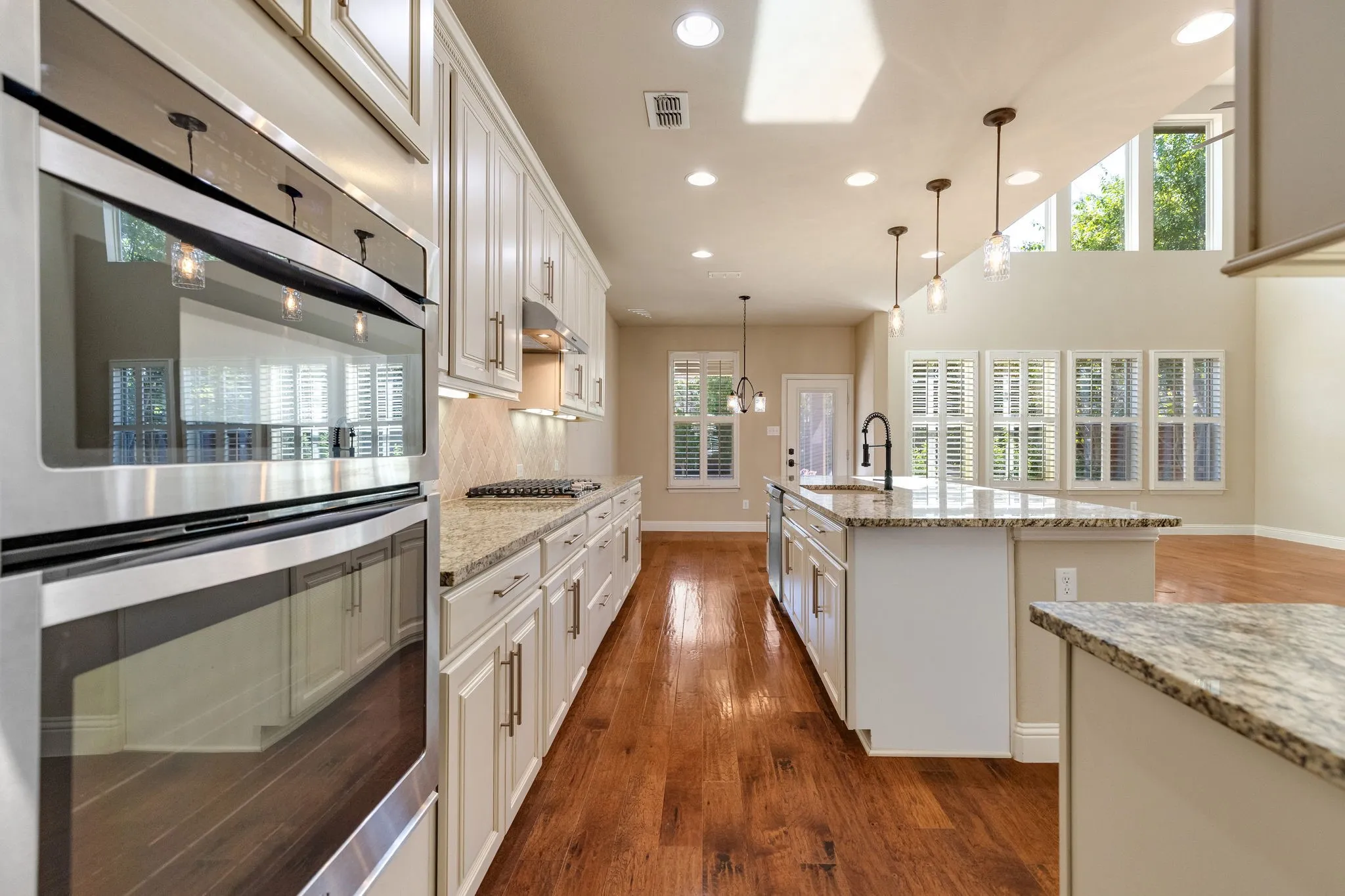Gourmet kitchen featuring stainless steel double ovens, a gas cooktop, granite countertops, wood-finish flooring, and white cabinetry with under-cabinet lighting