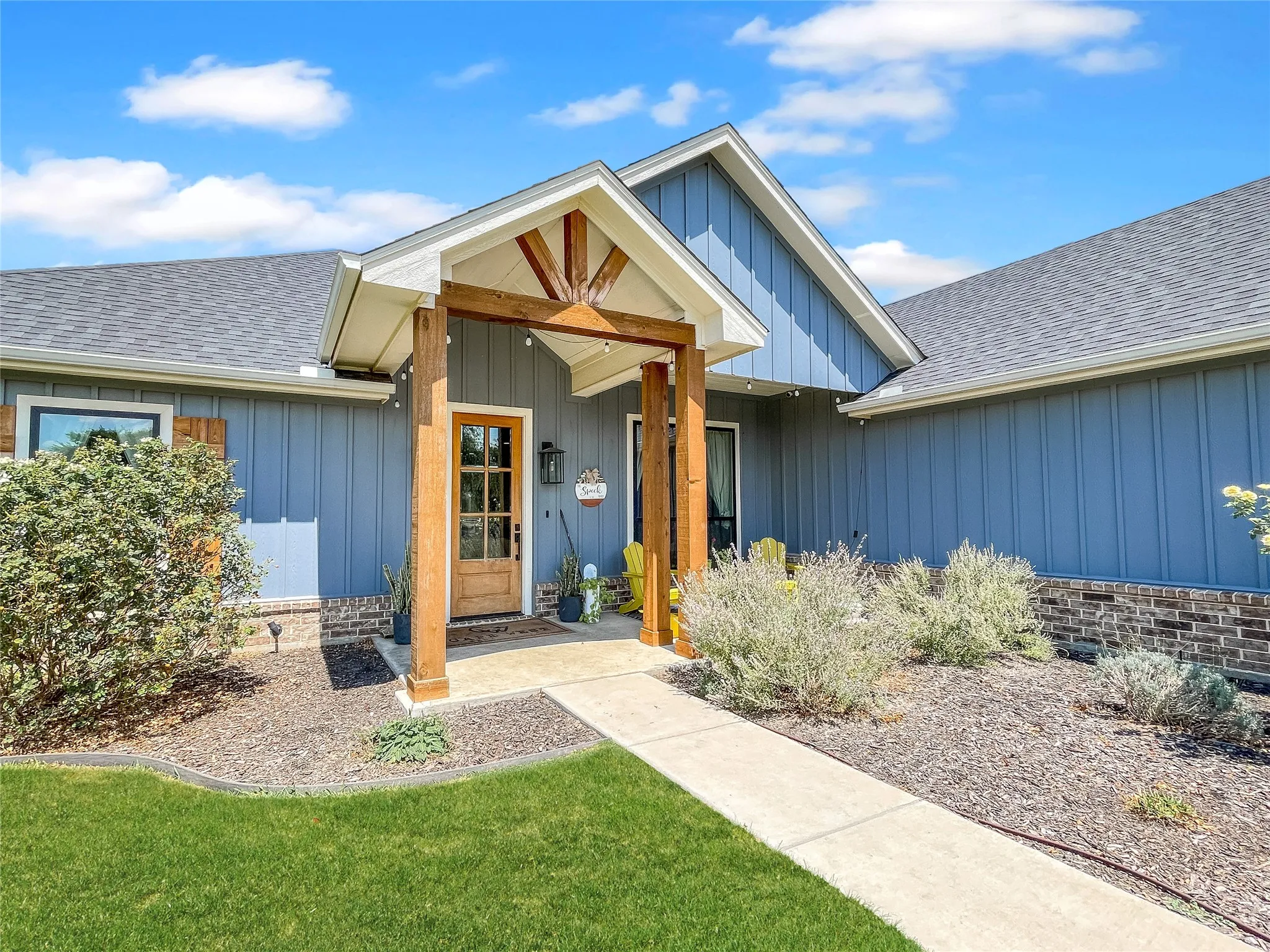 Board and batten siding, brick foundation, wood support beams, gabled roofline, and a concrete pathway