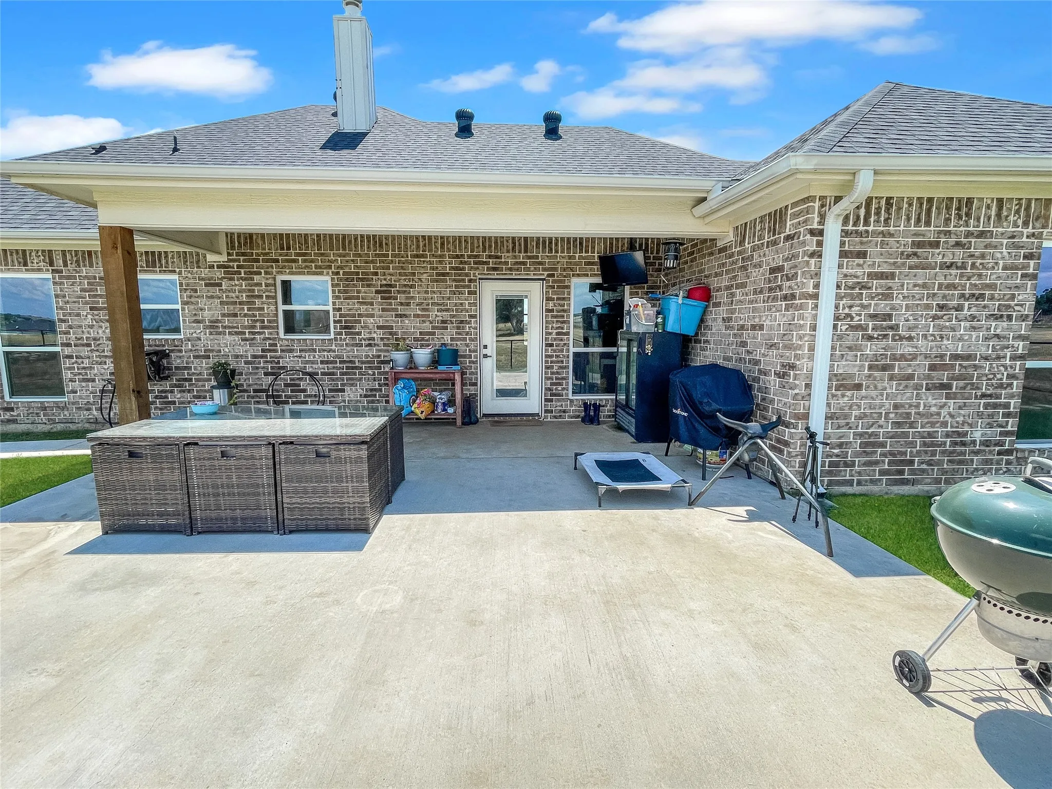 Expansive covered patio with concrete flooring, brick exterior, and a built-in outdoor sink