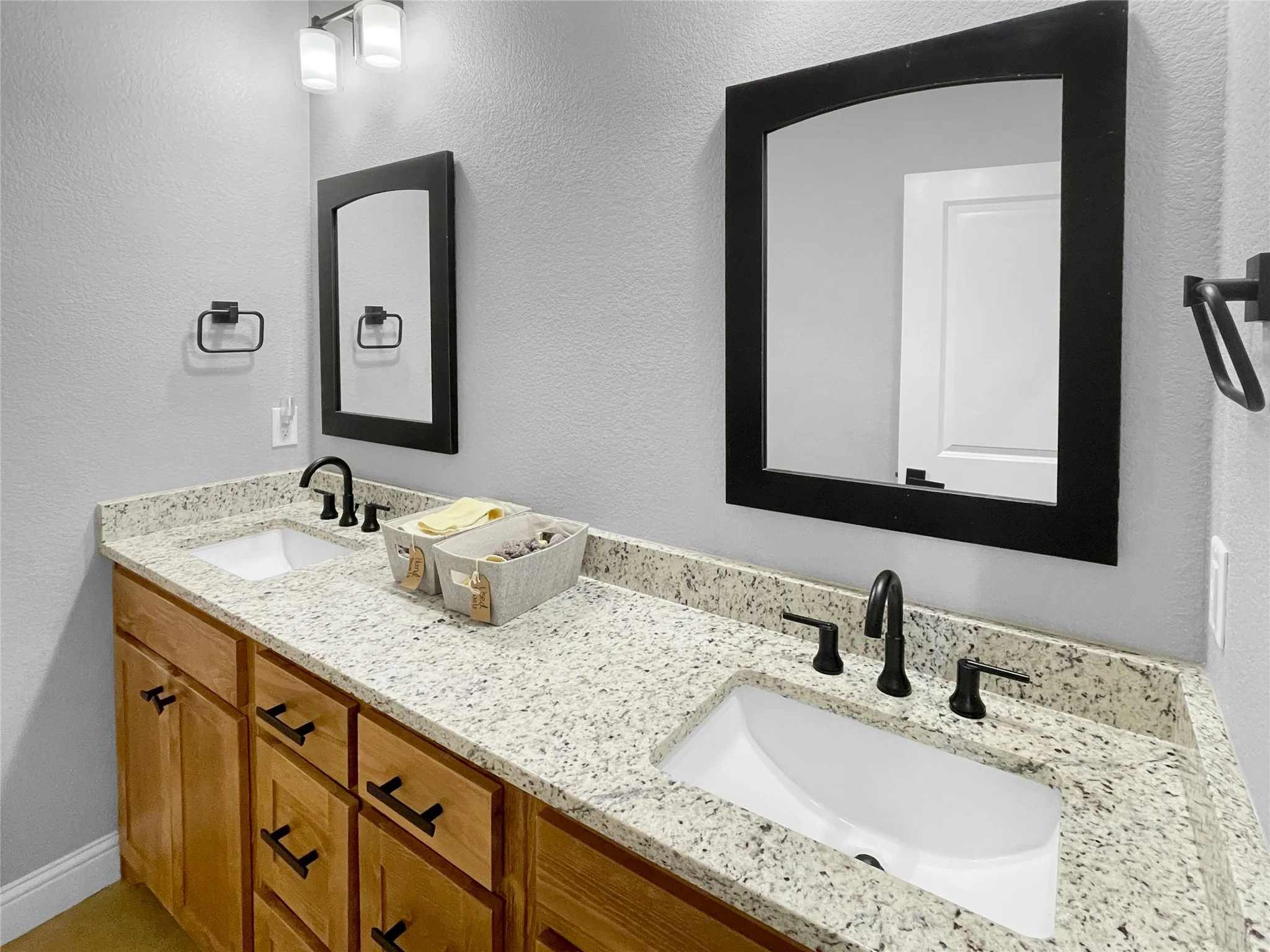 Double vanity with light-colored speckled countertop, undermount sinks, and matte black faucets