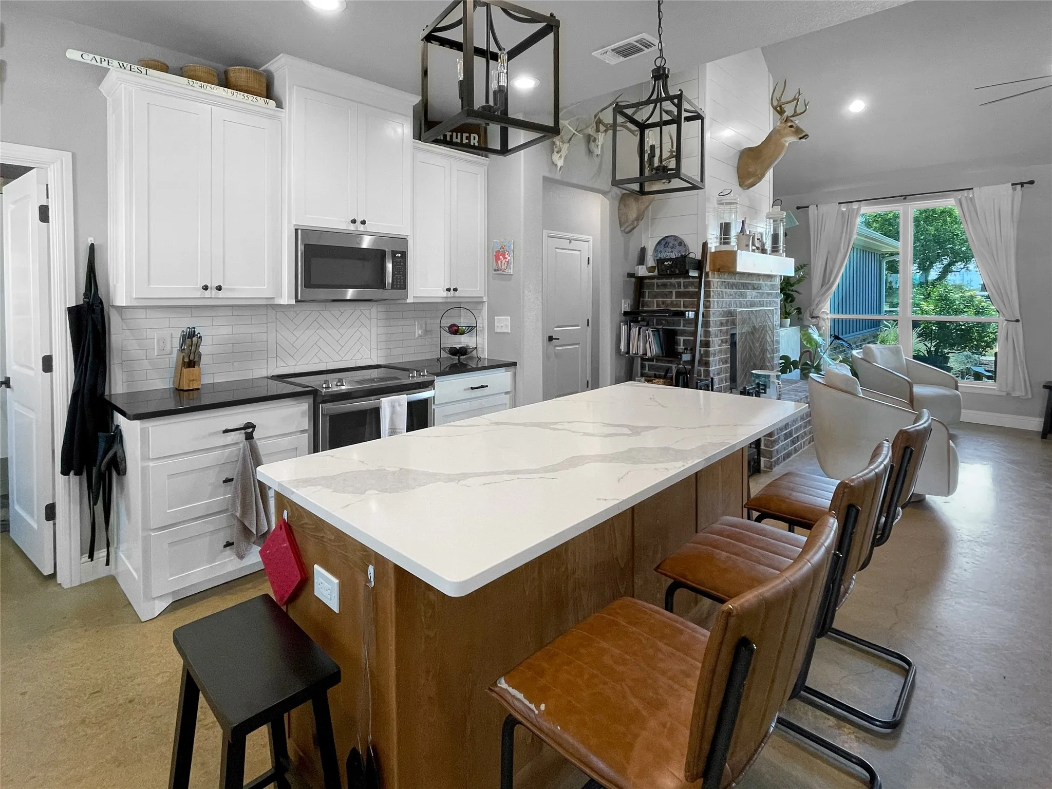 Kitchen featuring a large island with a light-toned countertop, white cabinetry with dark hardware, a subway tile backsplash, and stainless steel appliances