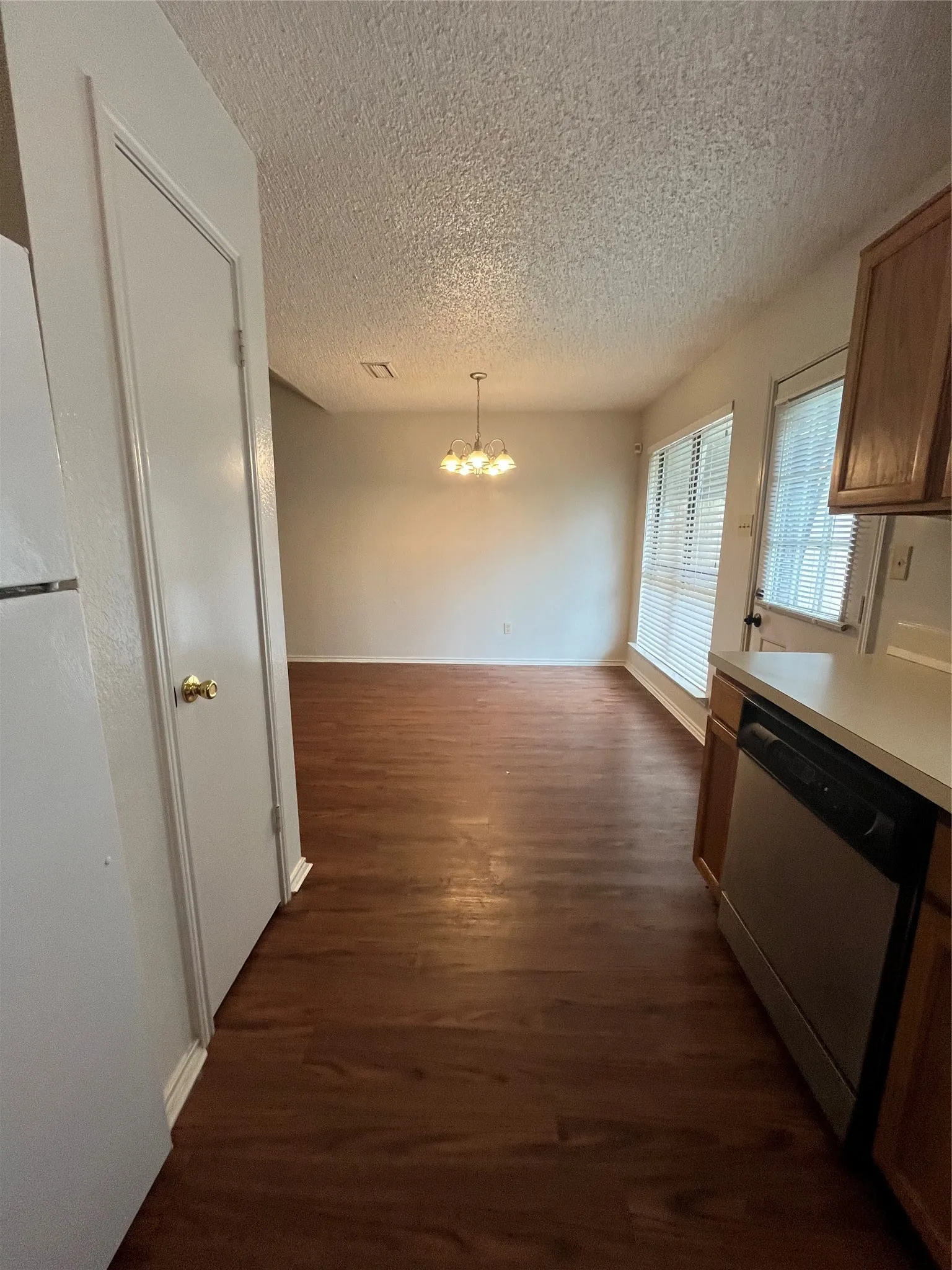 Kitchen with dishwashing machine, a chandelier, a textured ceiling, dark hardwood / wood-style flooring, and decorative light fixtures