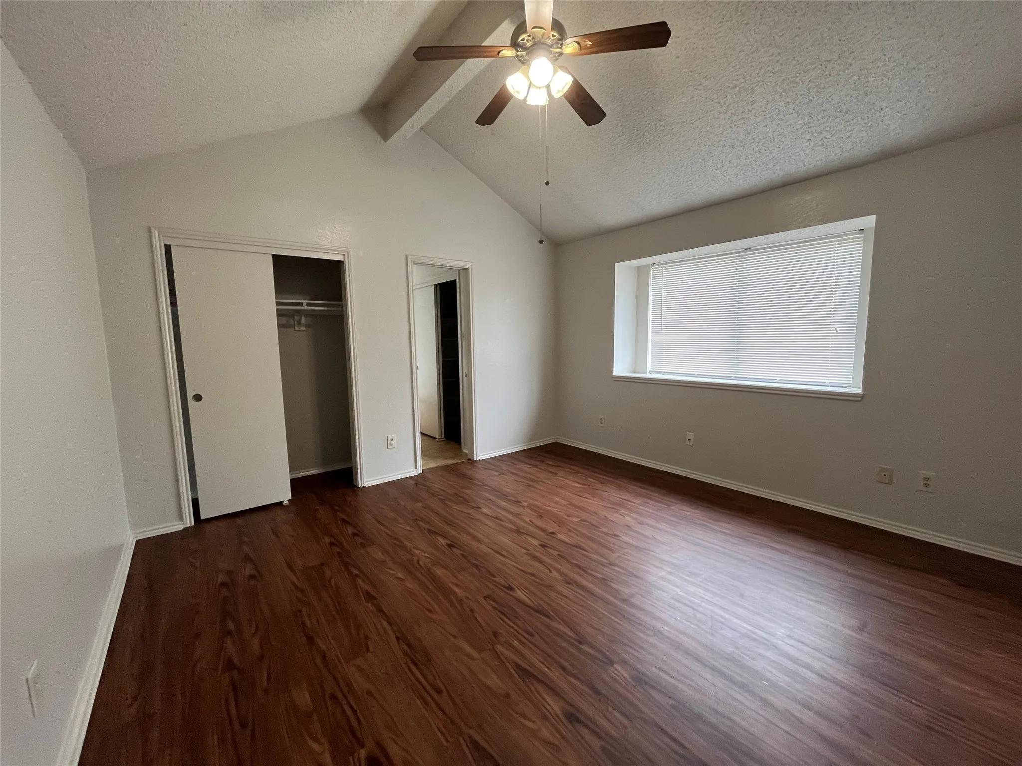 Unfurnished bedroom with vaulted ceiling with beams, a textured ceiling, dark hardwood / wood-style flooring, ceiling fan, and a closet