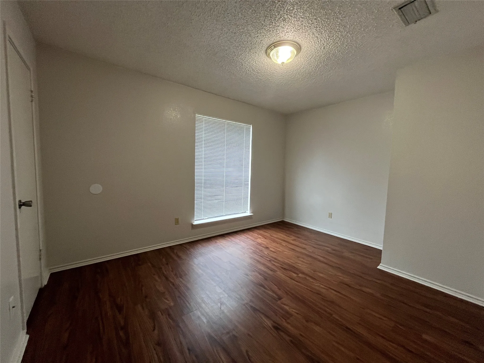 Empty room featuring dark hardwood / wood-style flooring and a textured ceiling