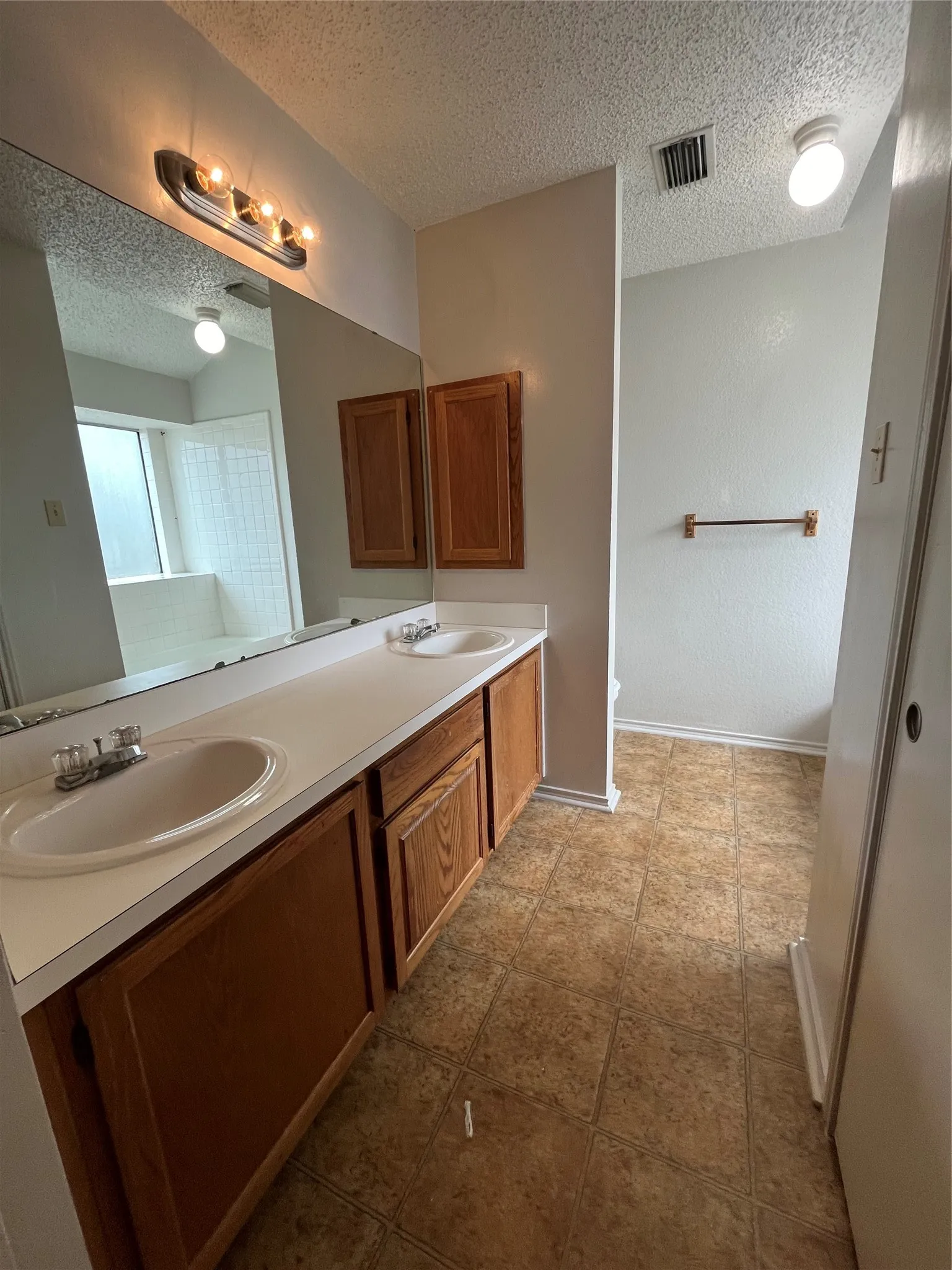 Bathroom featuring tile patterned floors, a textured ceiling, and dual bowl vanity