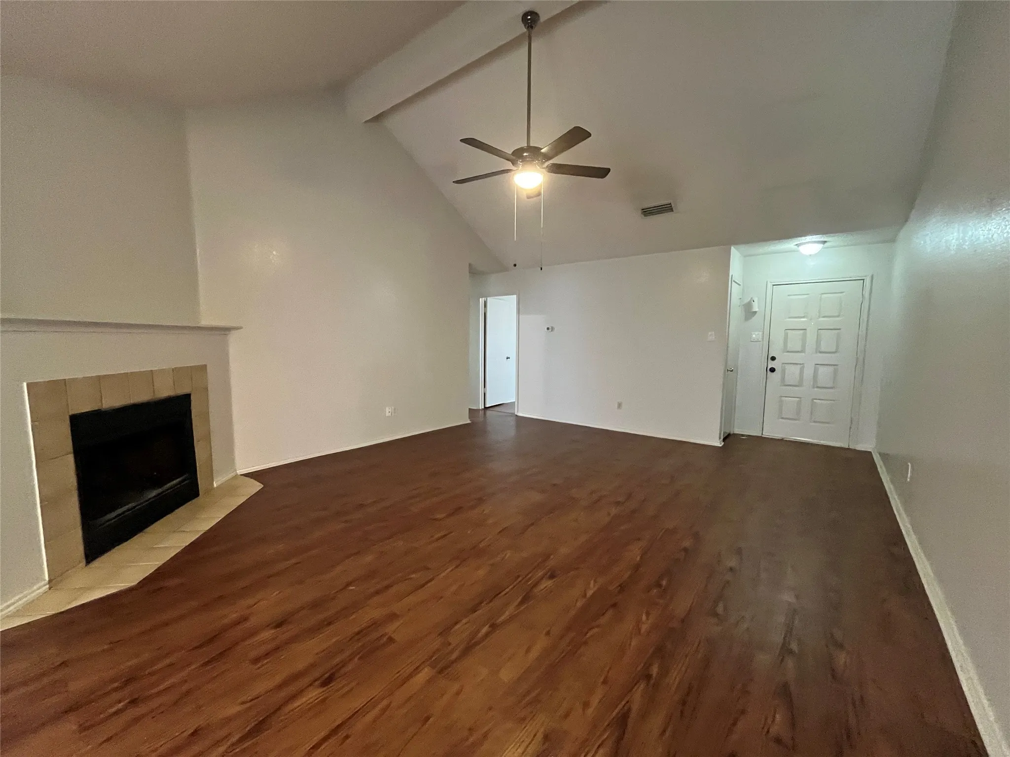 Unfurnished living room with vaulted ceiling with beams, ceiling fan, a fireplace, and hardwood / wood-style flooring