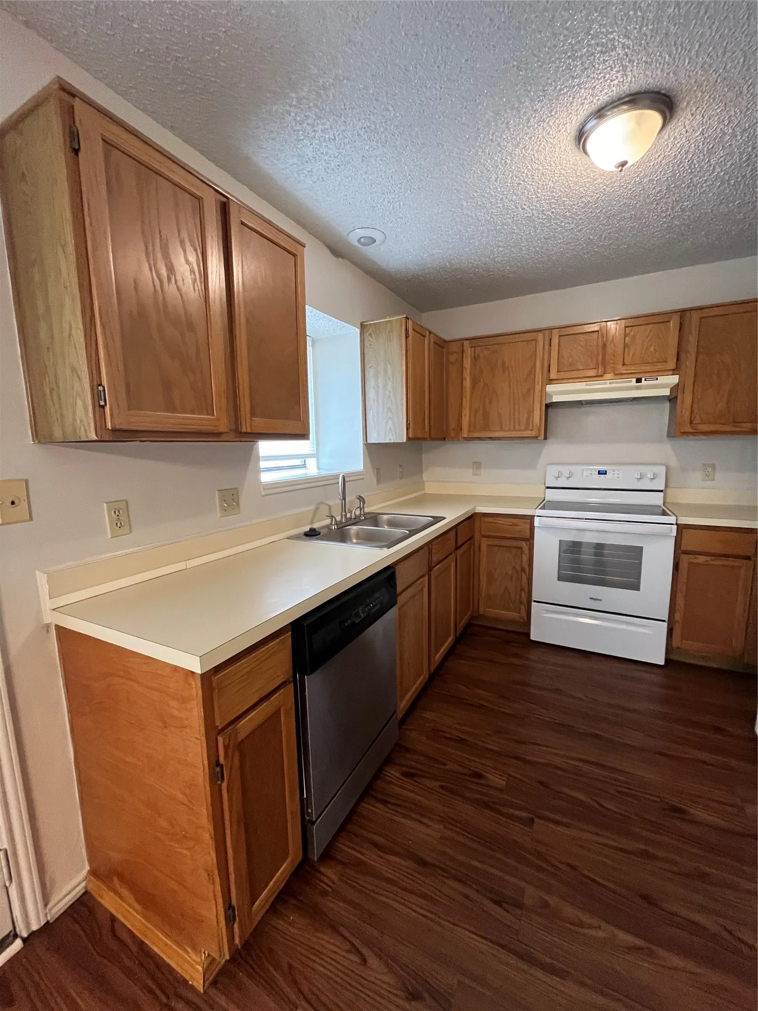 Kitchen with dishwashing machine, exhaust hood, range, and dark wood-type flooring