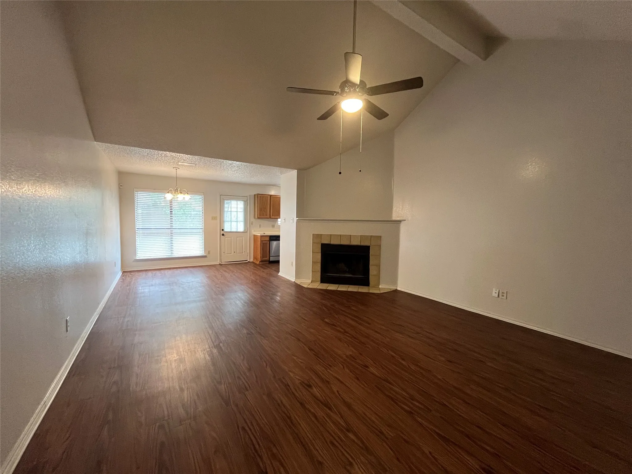 Unfurnished living room featuring beam ceiling, ceiling fan with notable chandelier, dark hardwood / wood-style flooring, a tile fireplace, and high vaulted ceiling