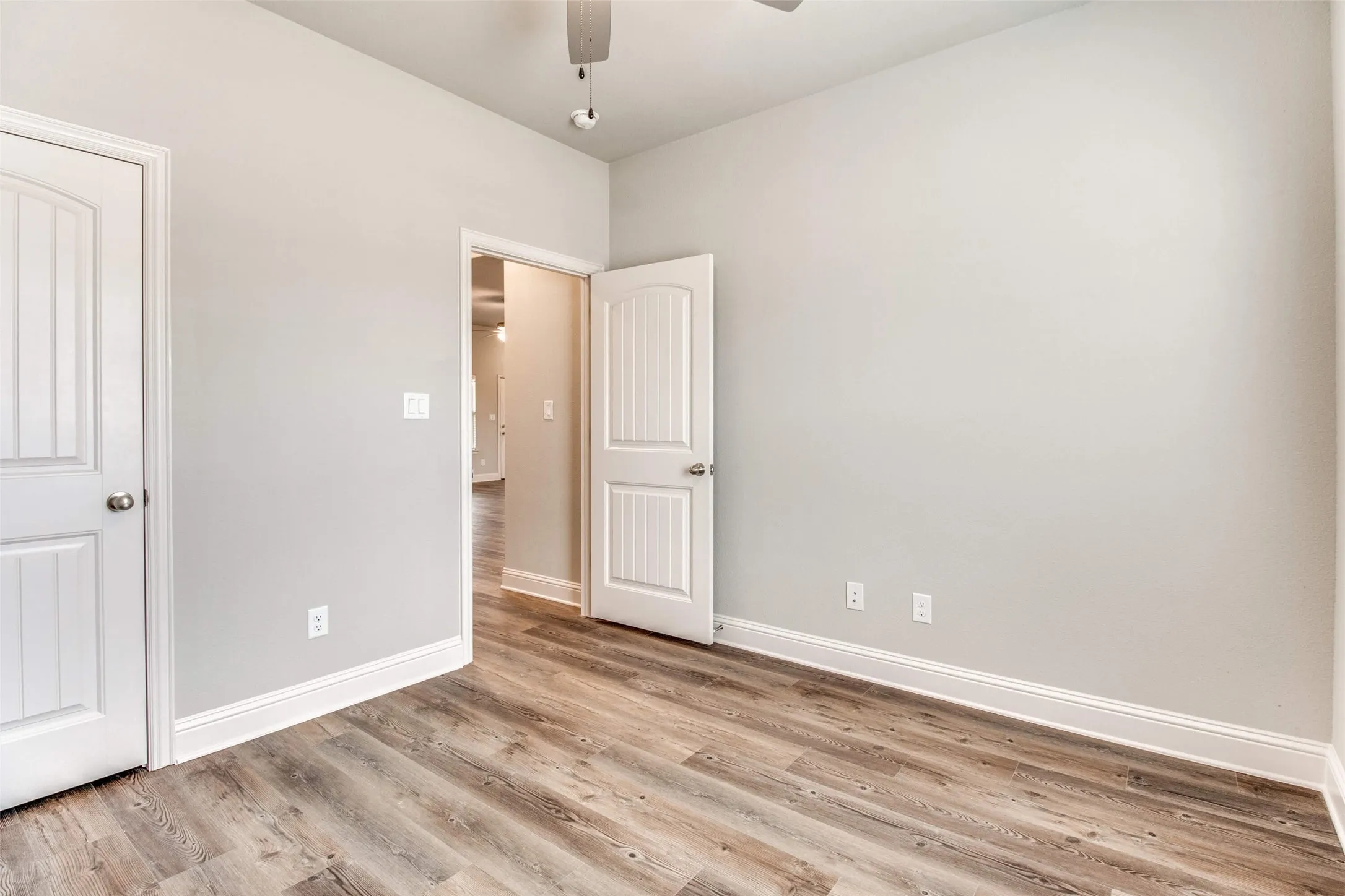 Wood-finish flooring, light gray wall paint, white trim, and white paneled doors