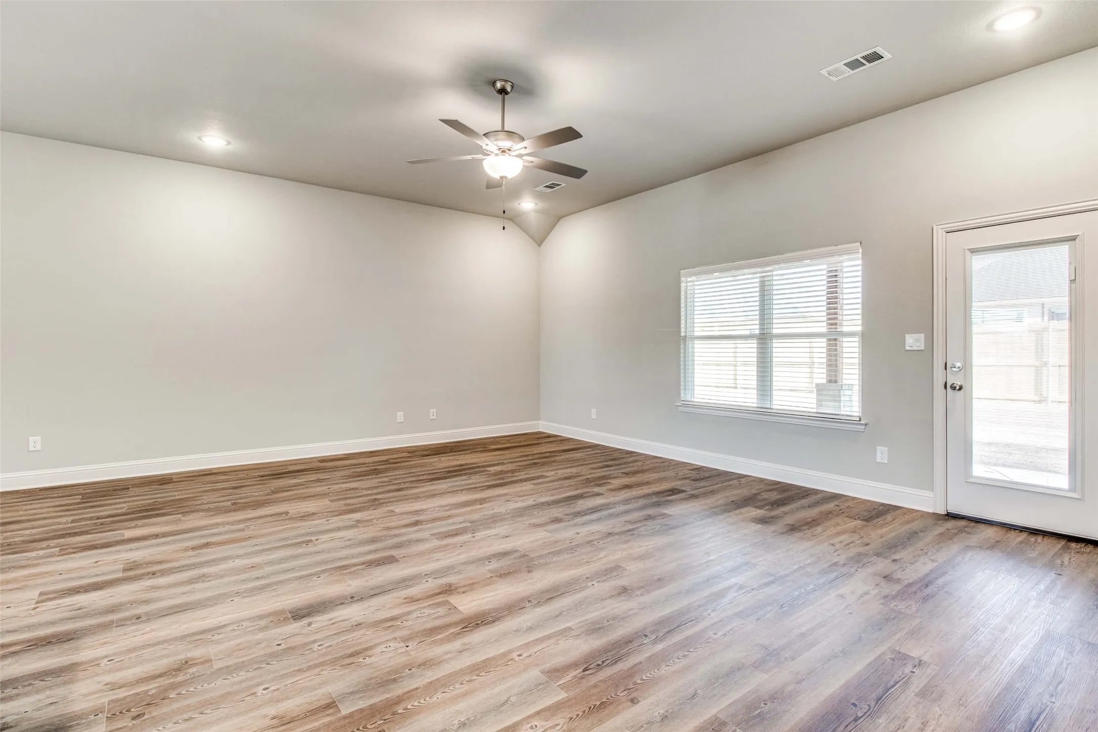 Wood-finish flooring, vaulted ceiling, recessed lighting, ceiling fan, and a glass-paned door