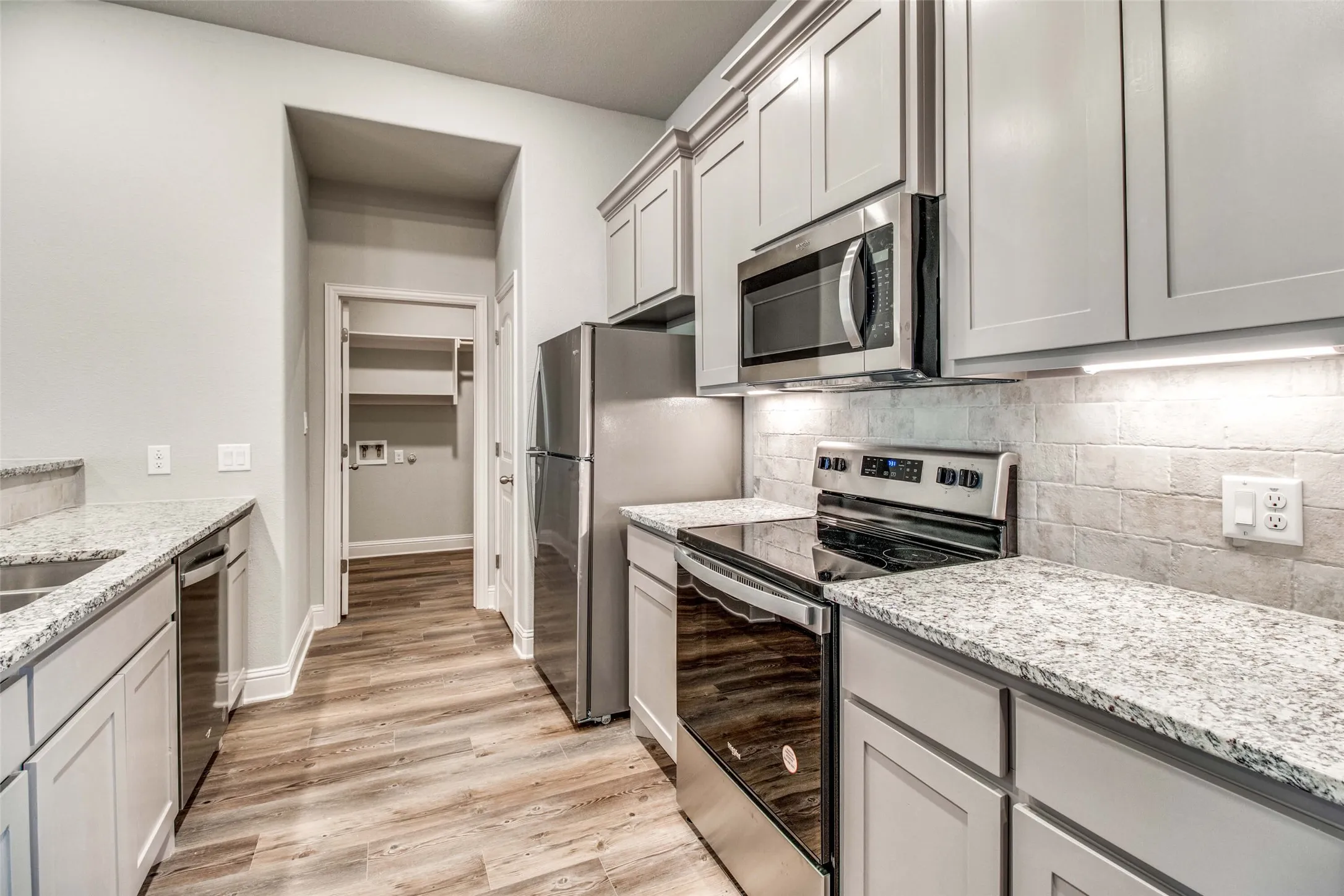 Stainless steel appliances, wood-finish flooring, light grey cabinetry, tile backsplash, and stone-finish countertops