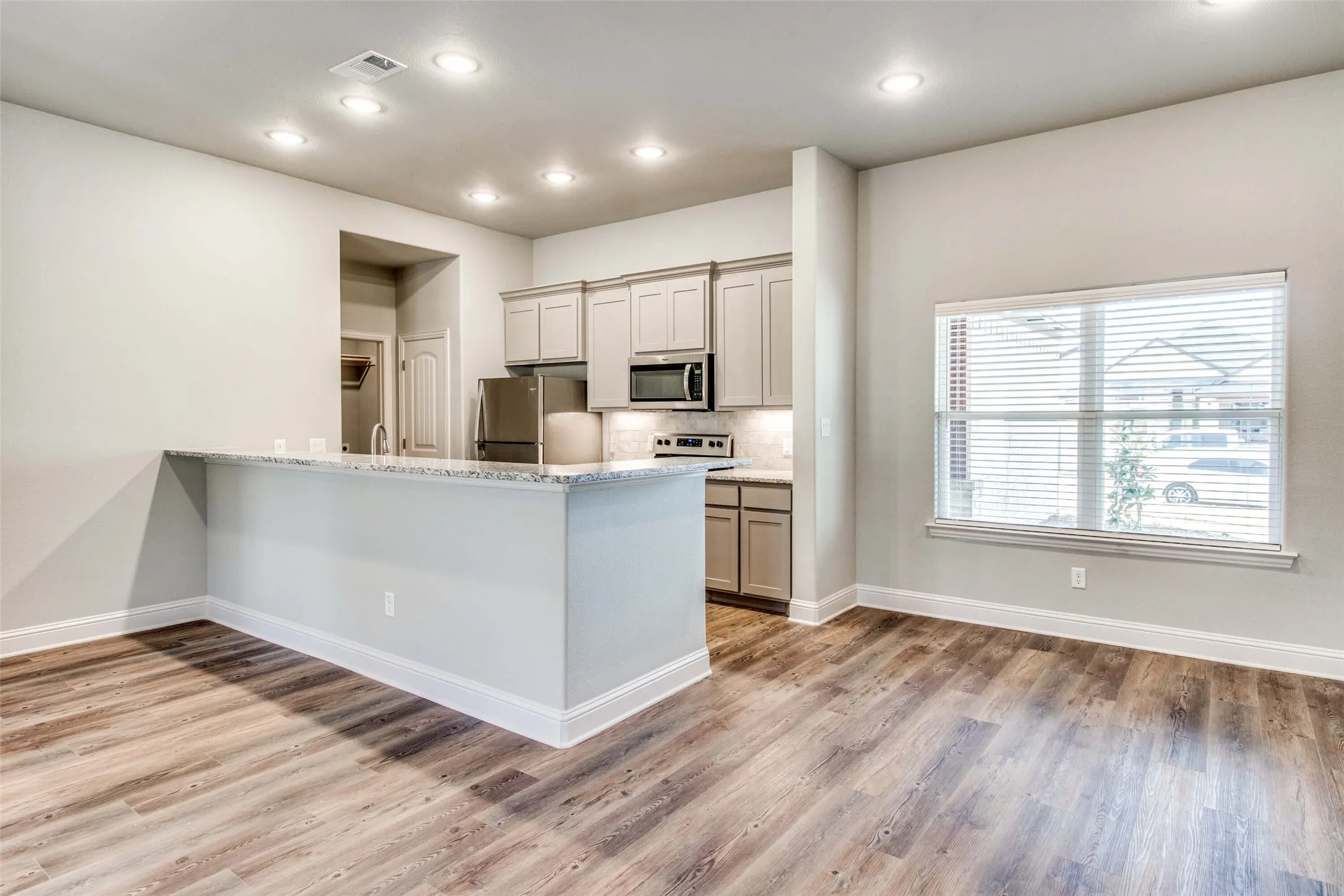 Wood-finish flooring throughout, recessed lighting, modern cabinetry, stainless steel appliances, and a stone-finish countertop