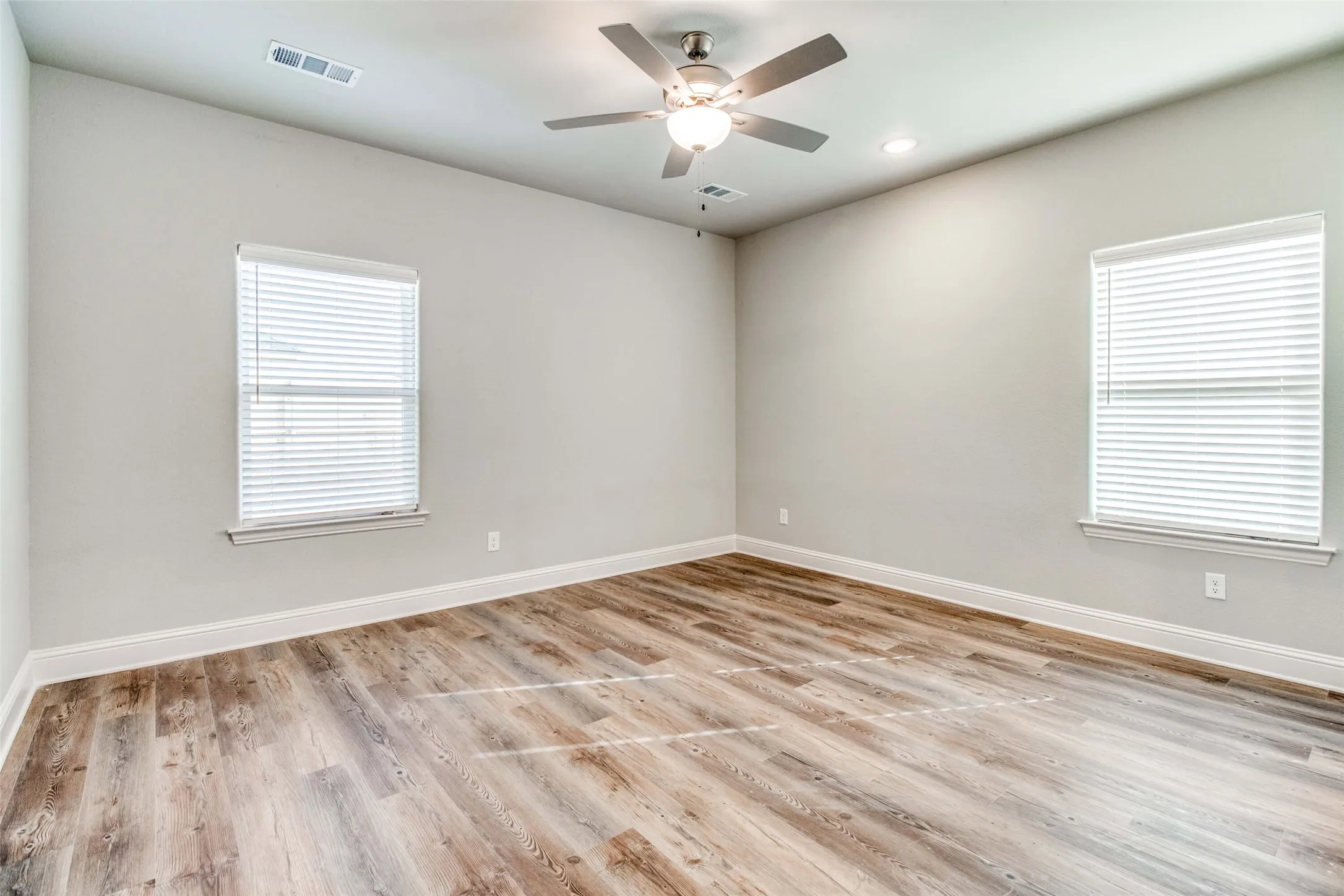 Wood-finish flooring, recessed lighting, ceiling fan with integrated light, and multiple windows with blinds