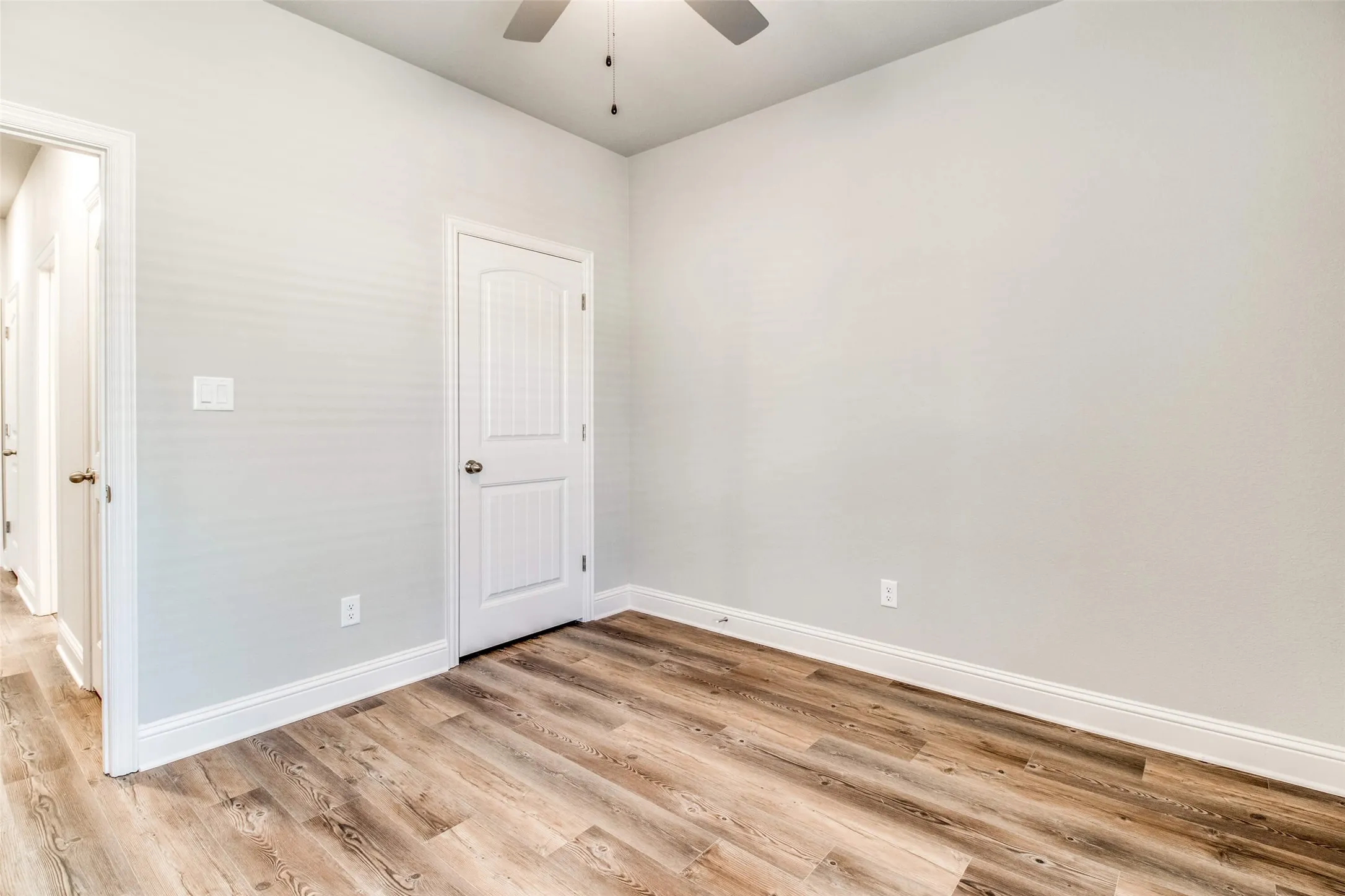 Wood-finish flooring, white trim, and a ceiling fan with integrated lighting