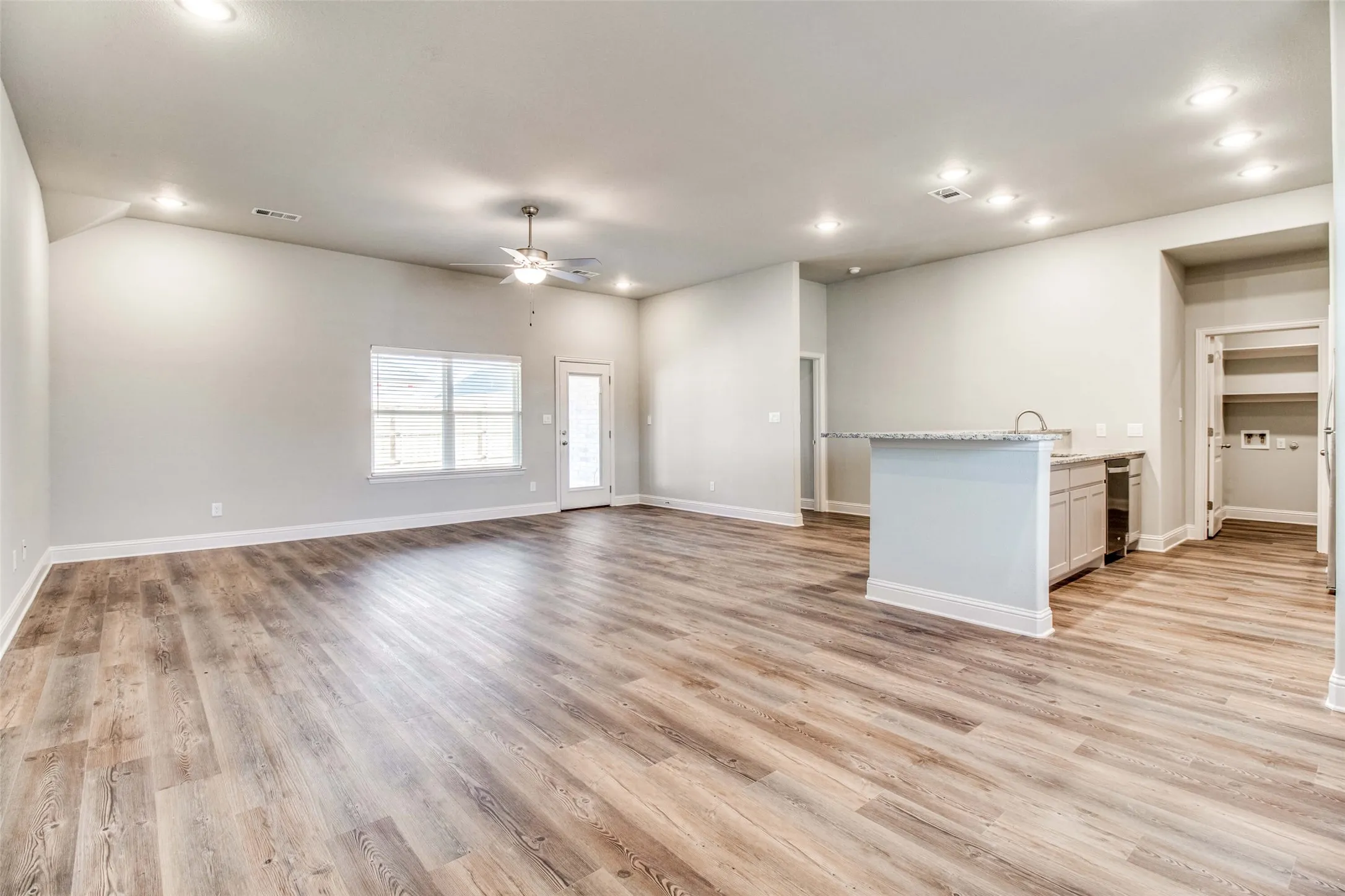 Vaulted ceiling with a ceiling fan, wood-finish flooring, recessed lighting, white window blinds, and a kitchen island with a sink and stone countertop