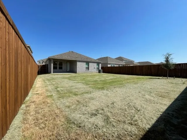 Expansive backyard featuring a privacy fence, a brick exterior, and a covered patio