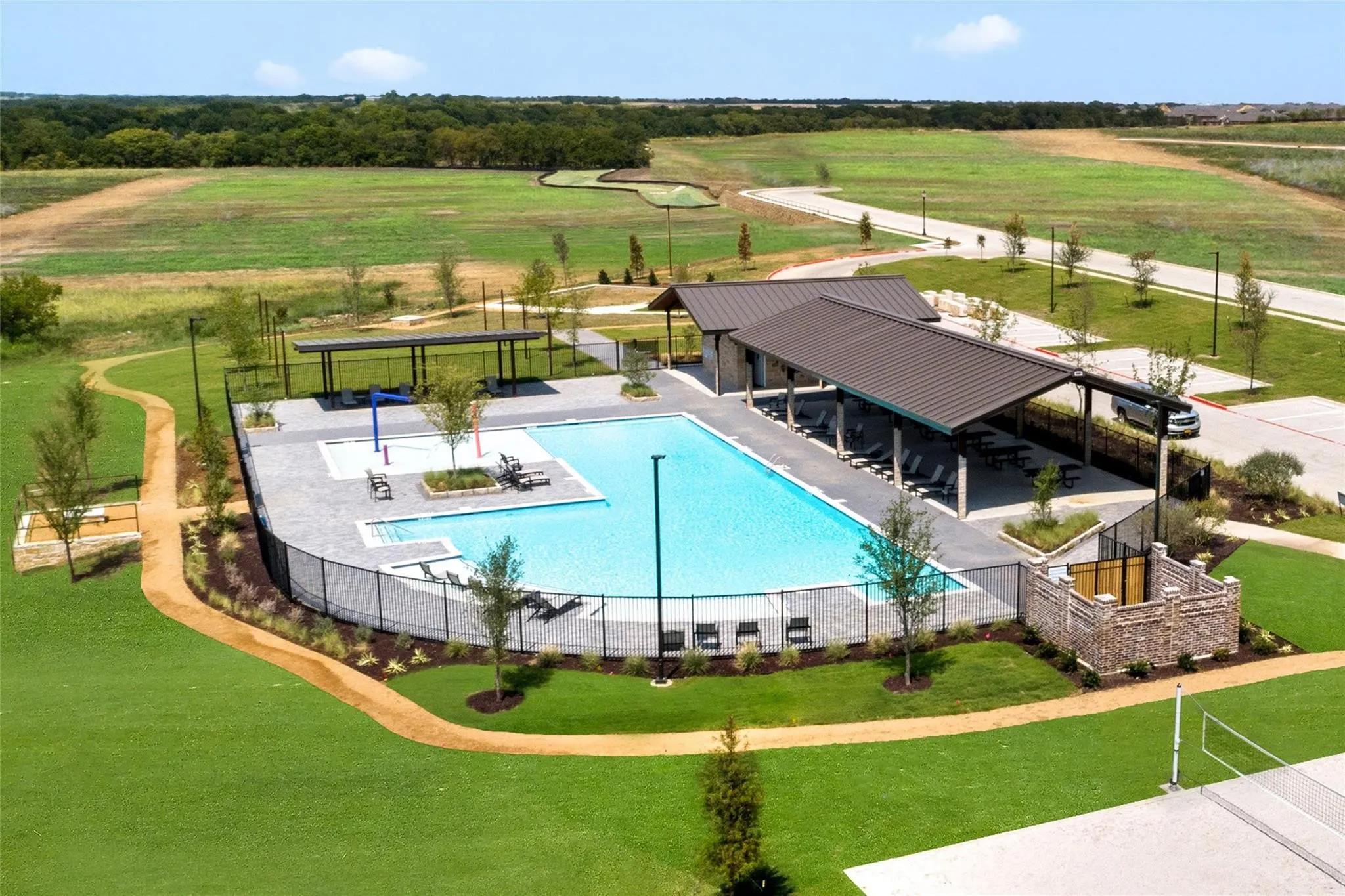 Community swimming pool with an expansive paver deck, covered lounge areas, and surrounding green spaces