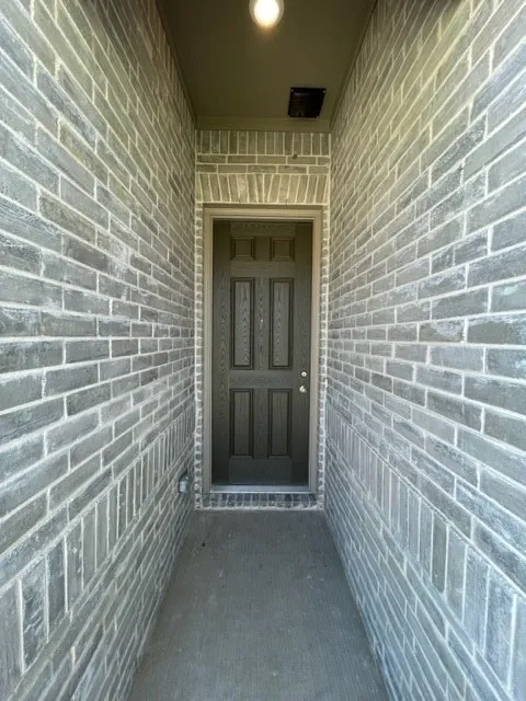 Brick exterior entry with an arched door frame, a paneled door, and an overhead light fixture