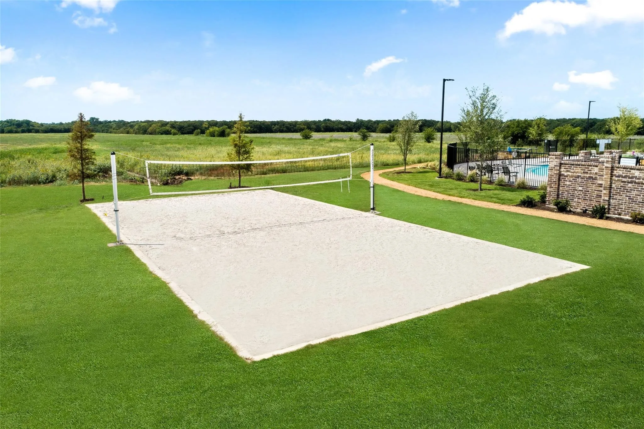 Sand volleyball court with a net, bordered by manicured lawn and a winding pathway