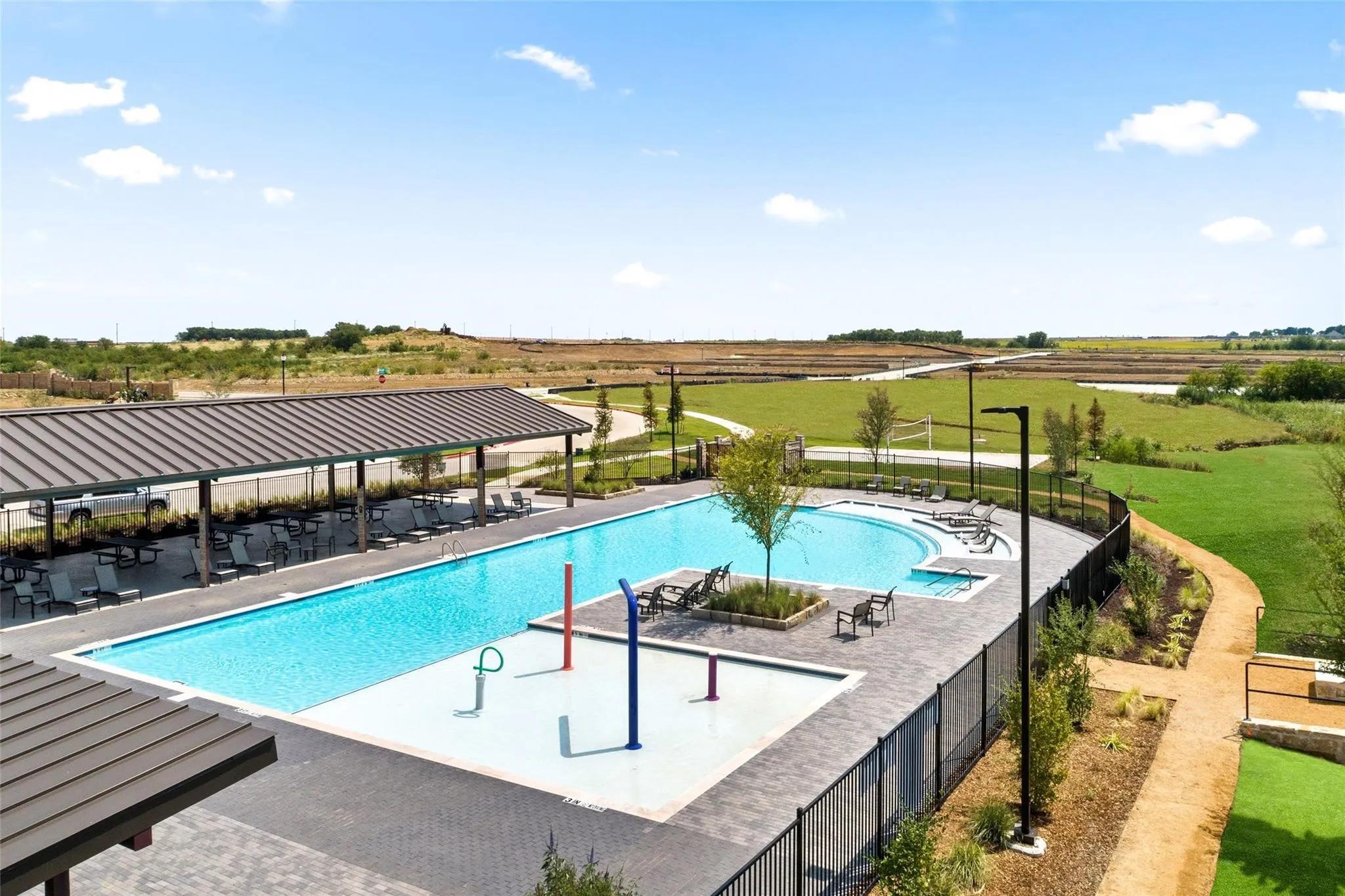 Expansive swimming pool with integrated splash pad, shaded poolside lounge area, and curved concrete walking paths