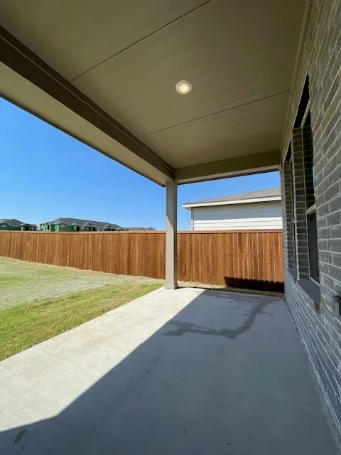 Covered concrete patio with recessed lighting, brick exterior, and a wood privacy fence