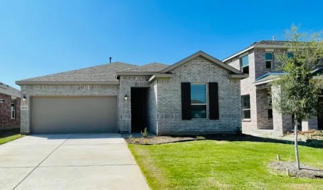 Gray brick exterior with dark shutters, attached garage, concrete driveway, and front lawn