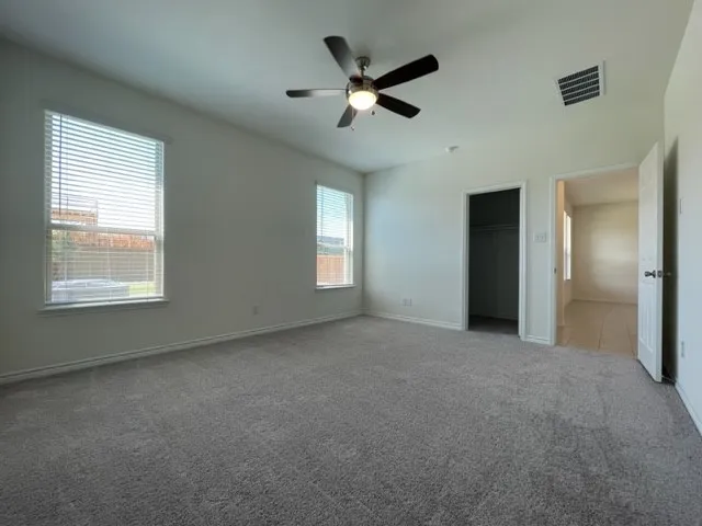 Spacious room featuring neutral carpet flooring, a ceiling fan with integrated lighting, and multiple windows