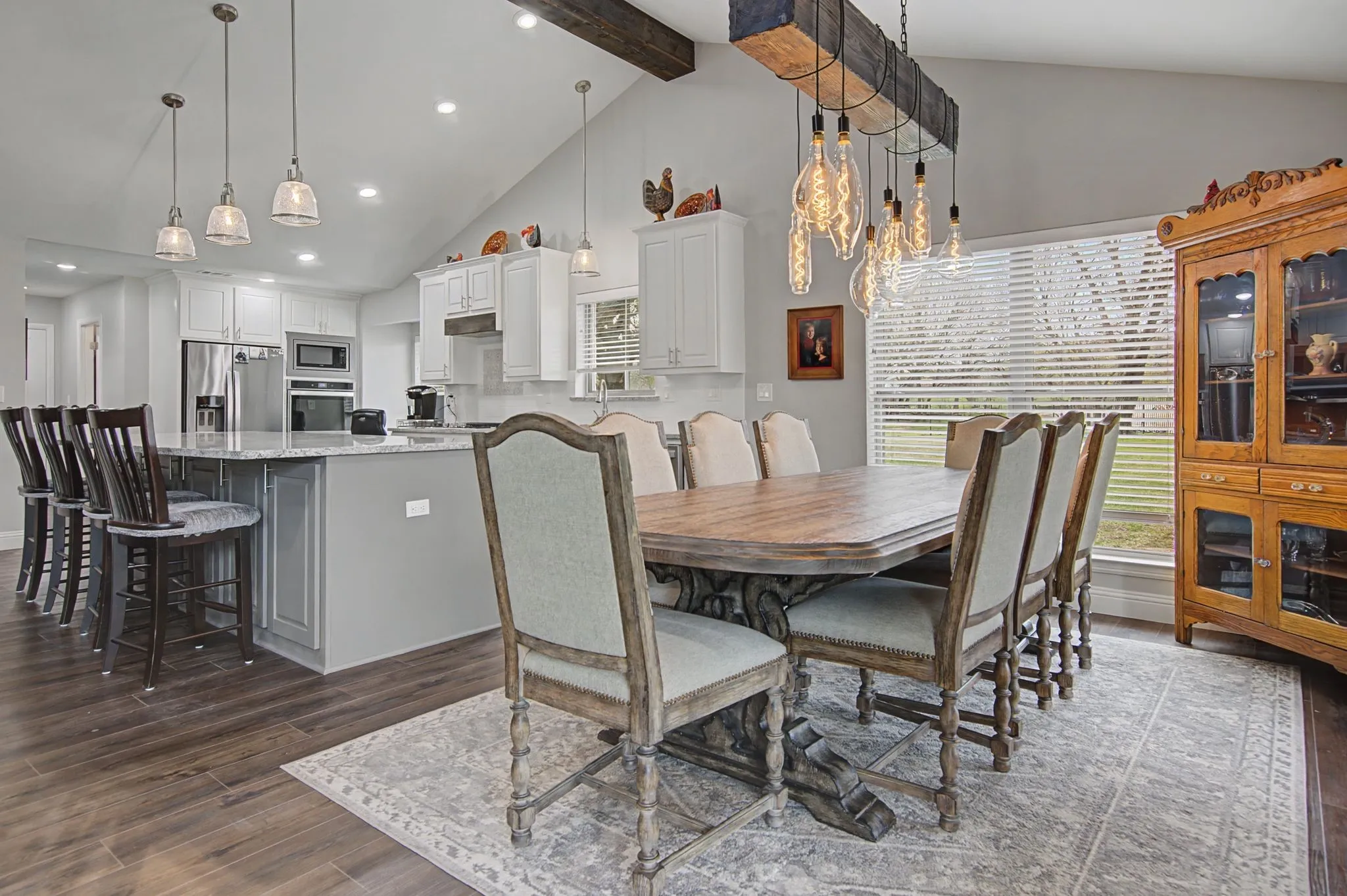 Vaulted ceiling with exposed wood beams, wood-finish flooring, recessed lighting, white cabinetry, and stainless steel appliances