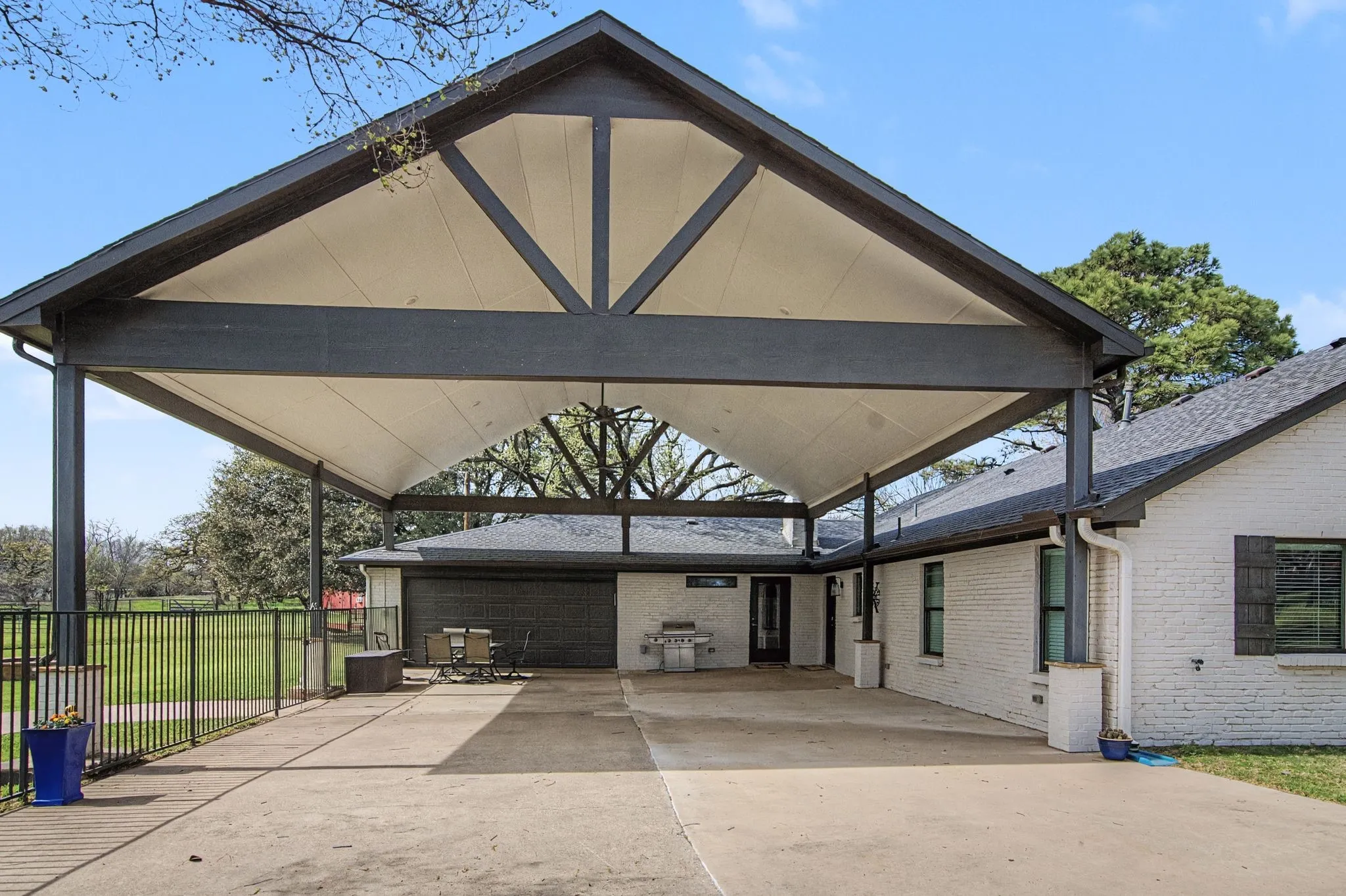 Expansive covered patio with exposed beam ceiling, concrete flooring, and an integrated outdoor cooking area