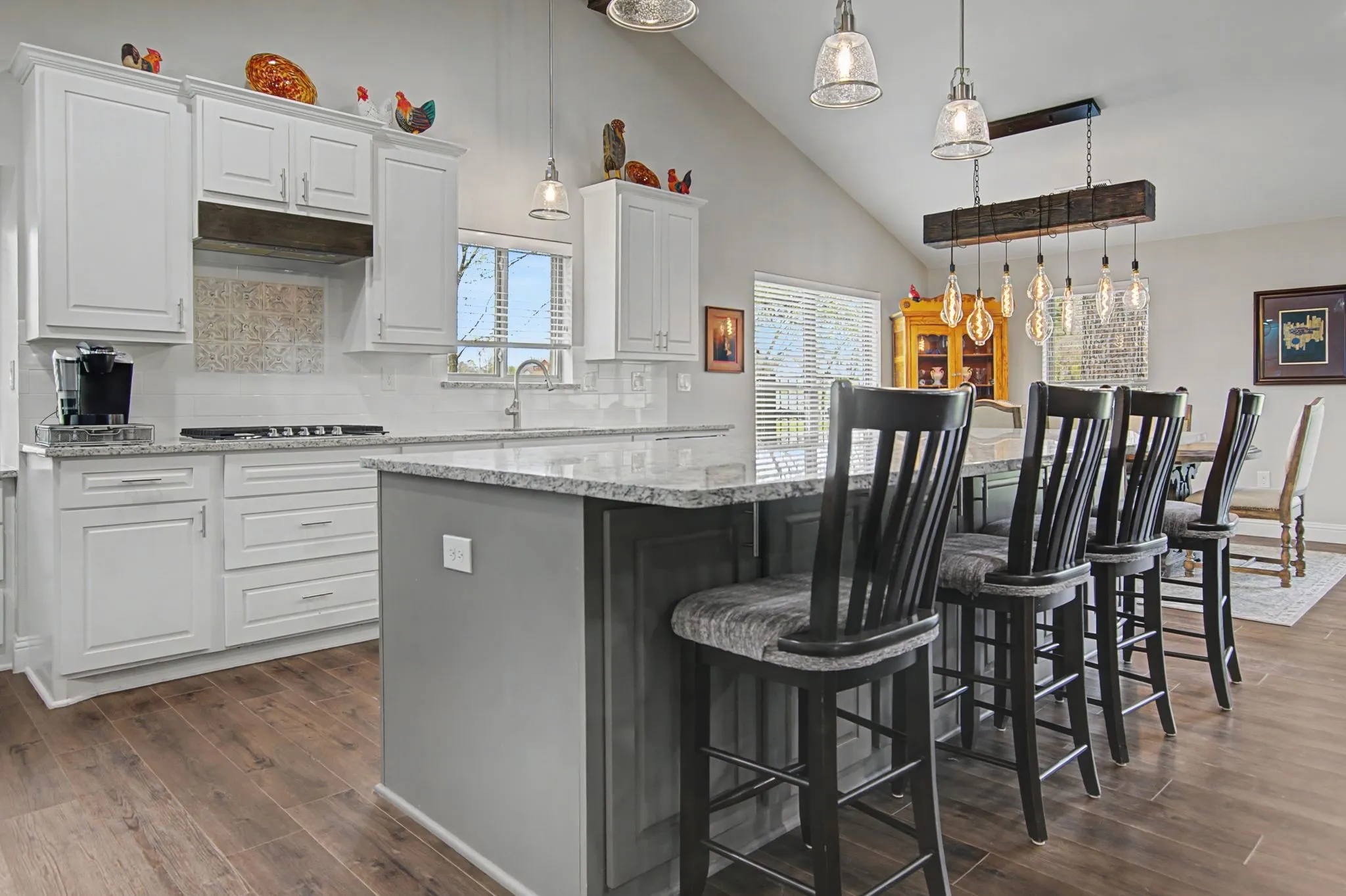 Vaulted ceiling kitchen featuring white cabinetry, granite countertops, a built-in gas cooktop, wood-finish flooring, and pendant lighting