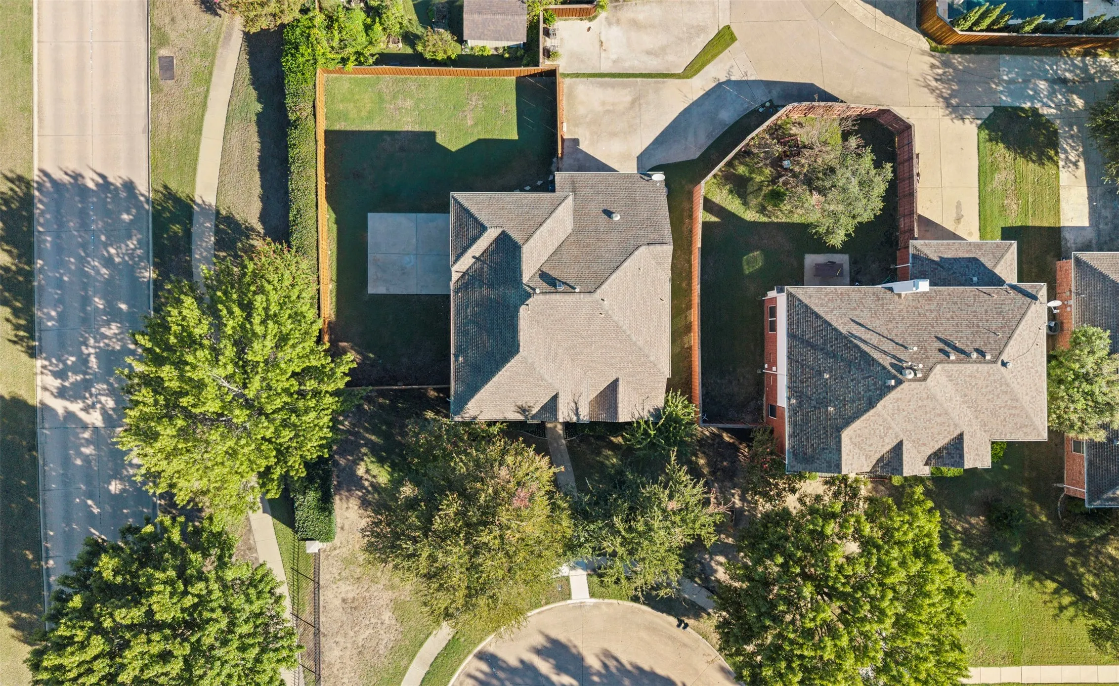 Pitched roof architecture, paved driveway, landscaped yard, concrete patio, and mature perimeter trees