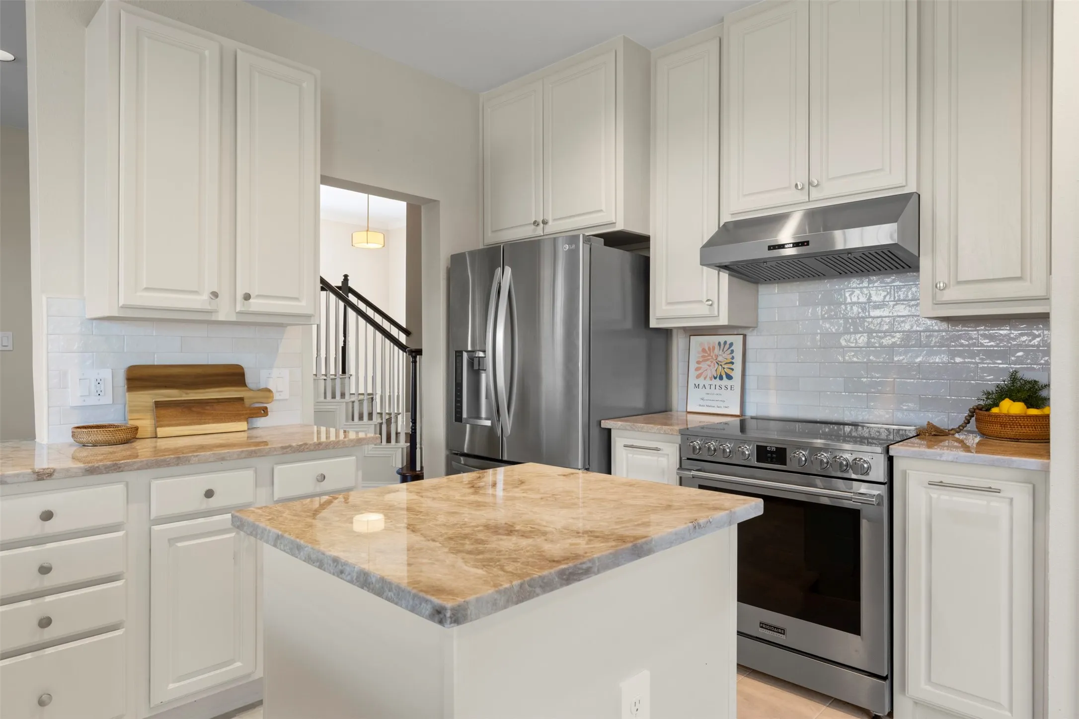 Kitchen featuring white cabinetry, stainless steel appliances, a tile backsplash, light-toned countertops, and a central island