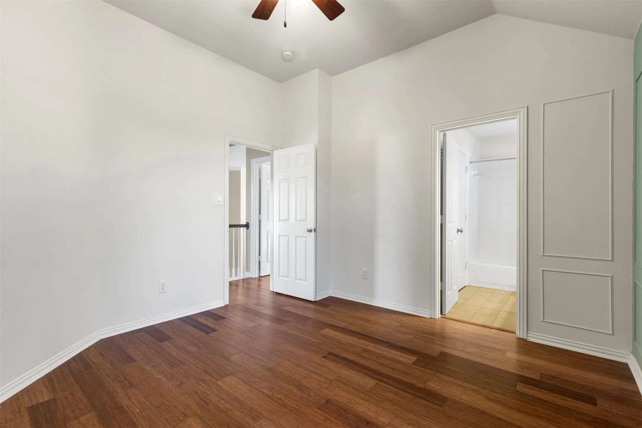 Vaulted ceiling with a wood-finish ceiling fan, wood-finish flooring, and white paneled interior doors