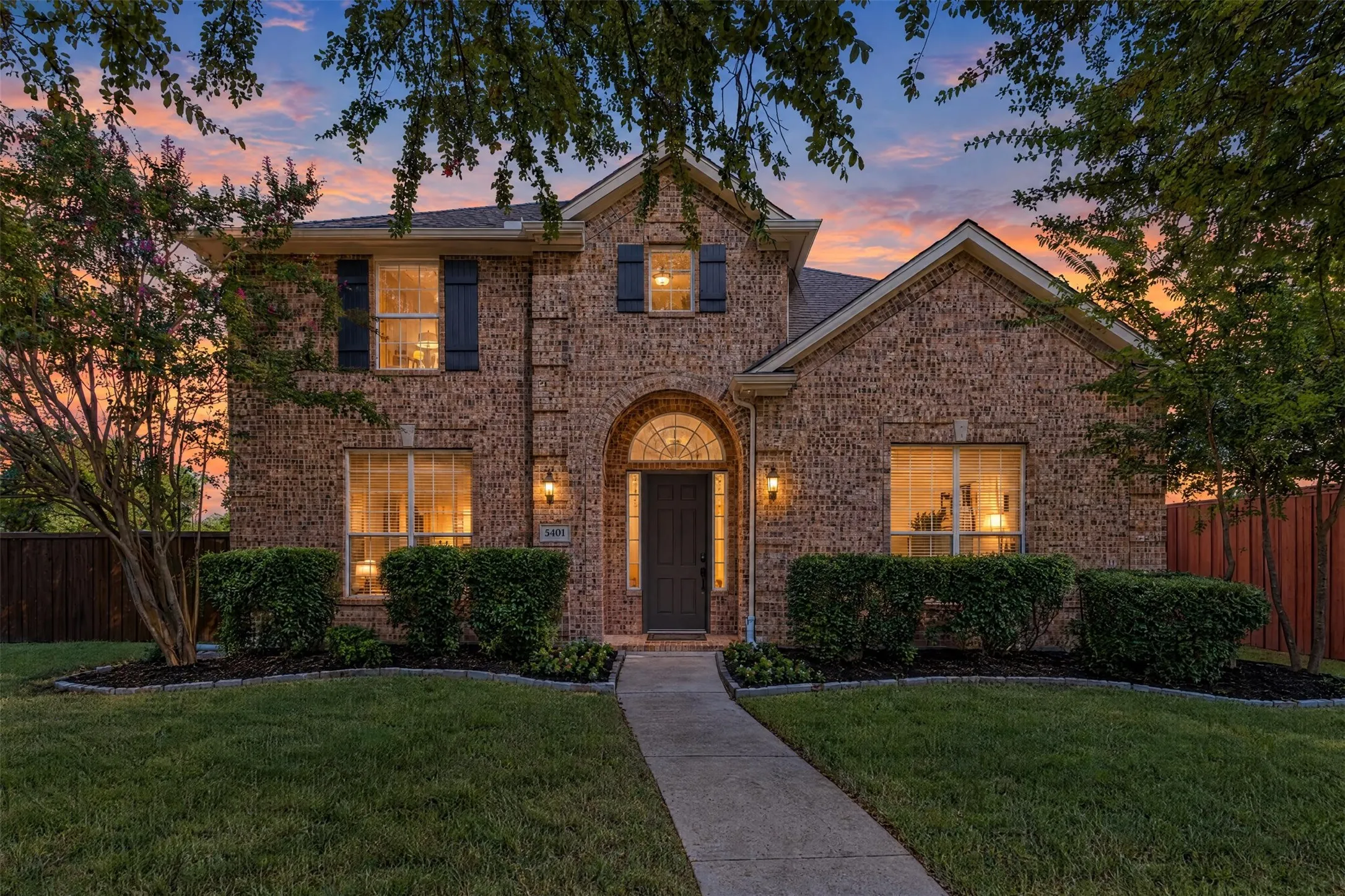 Brick exterior, arched entry, formal landscaping, front walkway, and mature trees