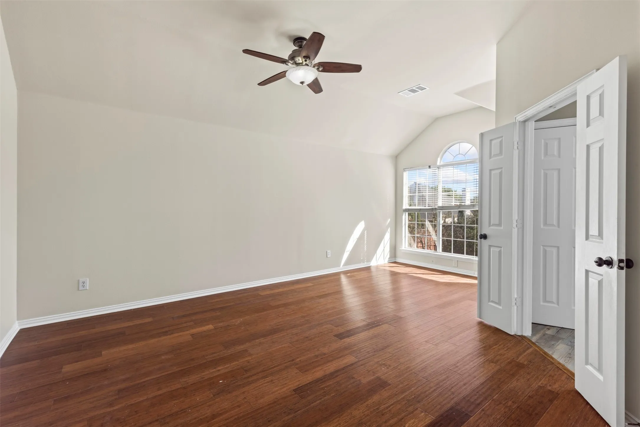 Wood-finish flooring, vaulted ceiling, arched window, ceiling fan, and white panel doors
