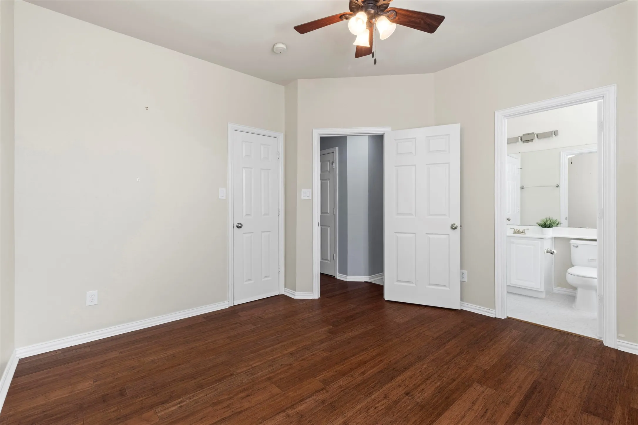 Wood-finish flooring, ceiling fan with integrated lighting, white interior doors, and a bathroom featuring a vanity with a white countertop and a toilet