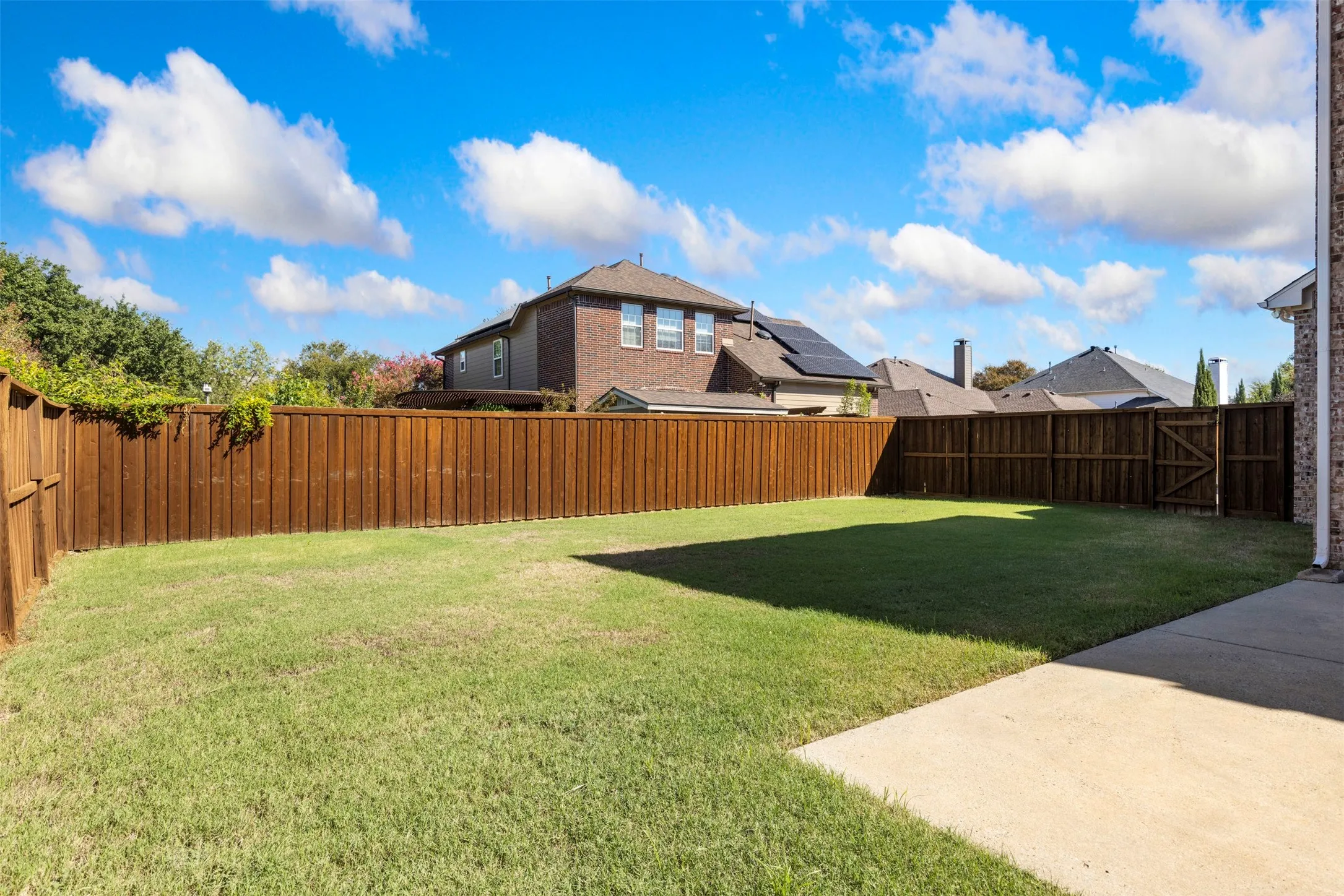 Expansive grassy backyard featuring a perimeter wood fence, concrete patio, and a wood gate