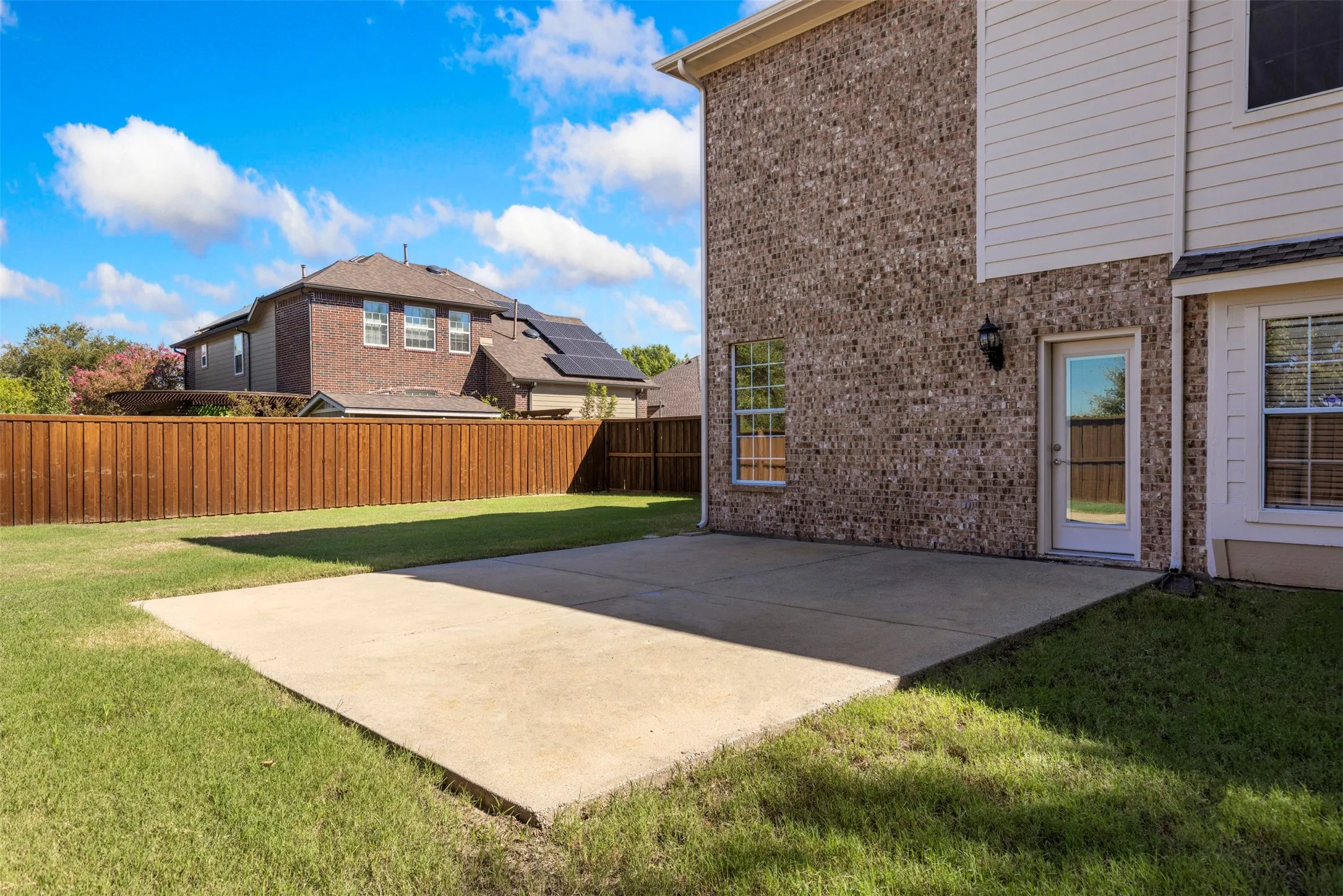 Expansive concrete patio with a manicured lawn, brick and siding exterior, and a privacy fence