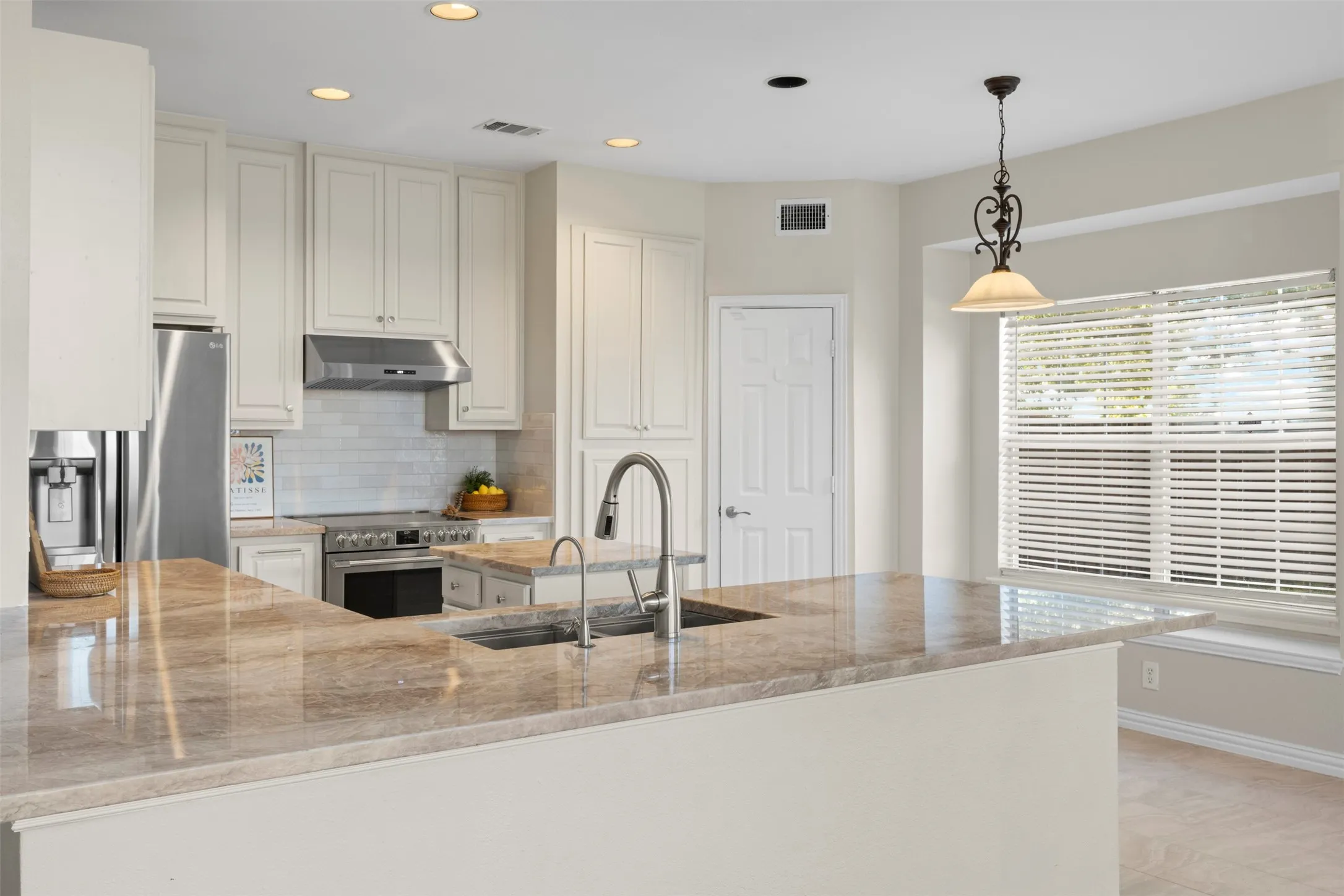 Spacious kitchen featuring an expansive island with a double basin sink, light-toned cabinetry, stainless steel range with overhead hood, and recessed lighting