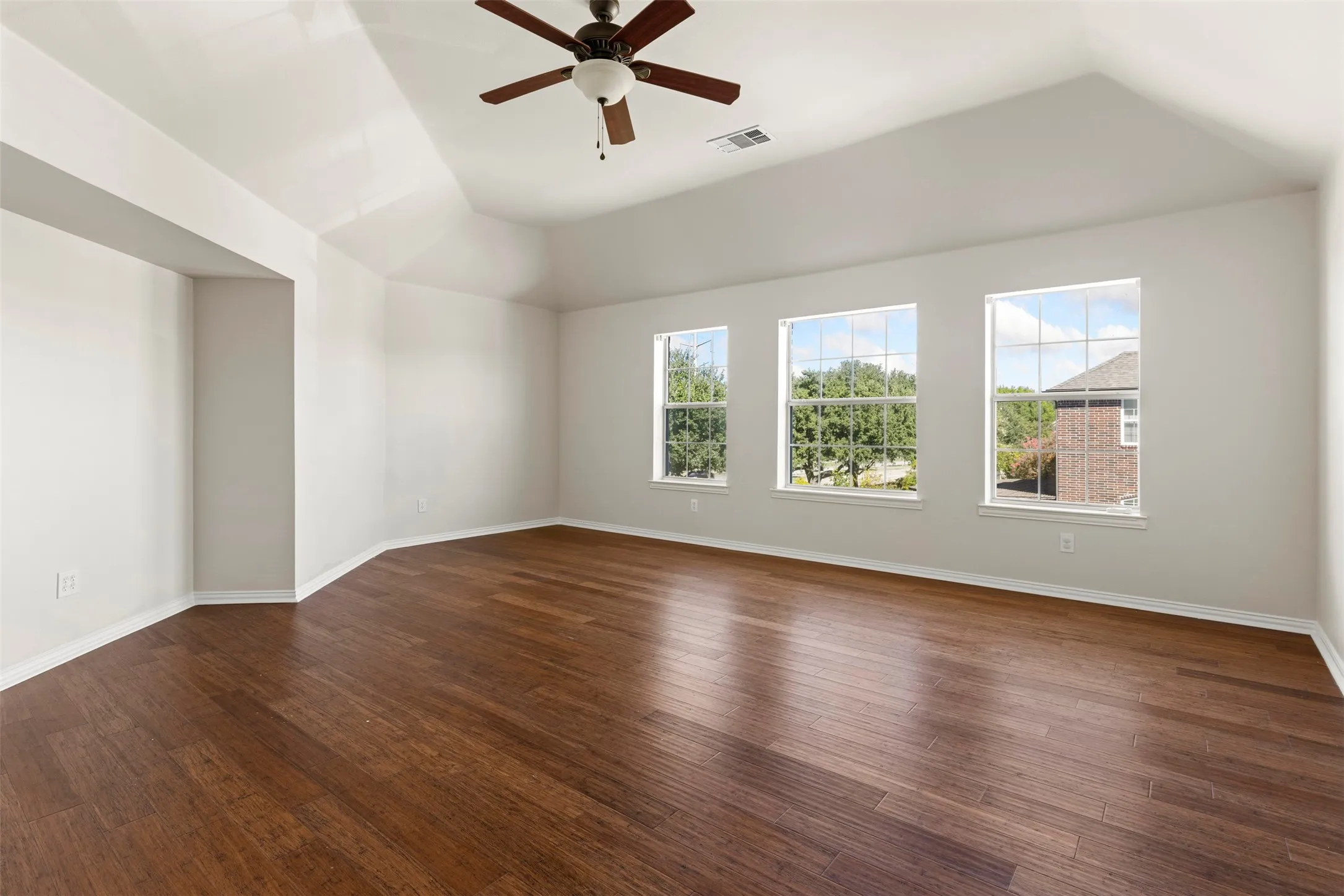 Vaulted ceiling with a ceiling fan, three windows, wood-finish flooring, and white painted walls
