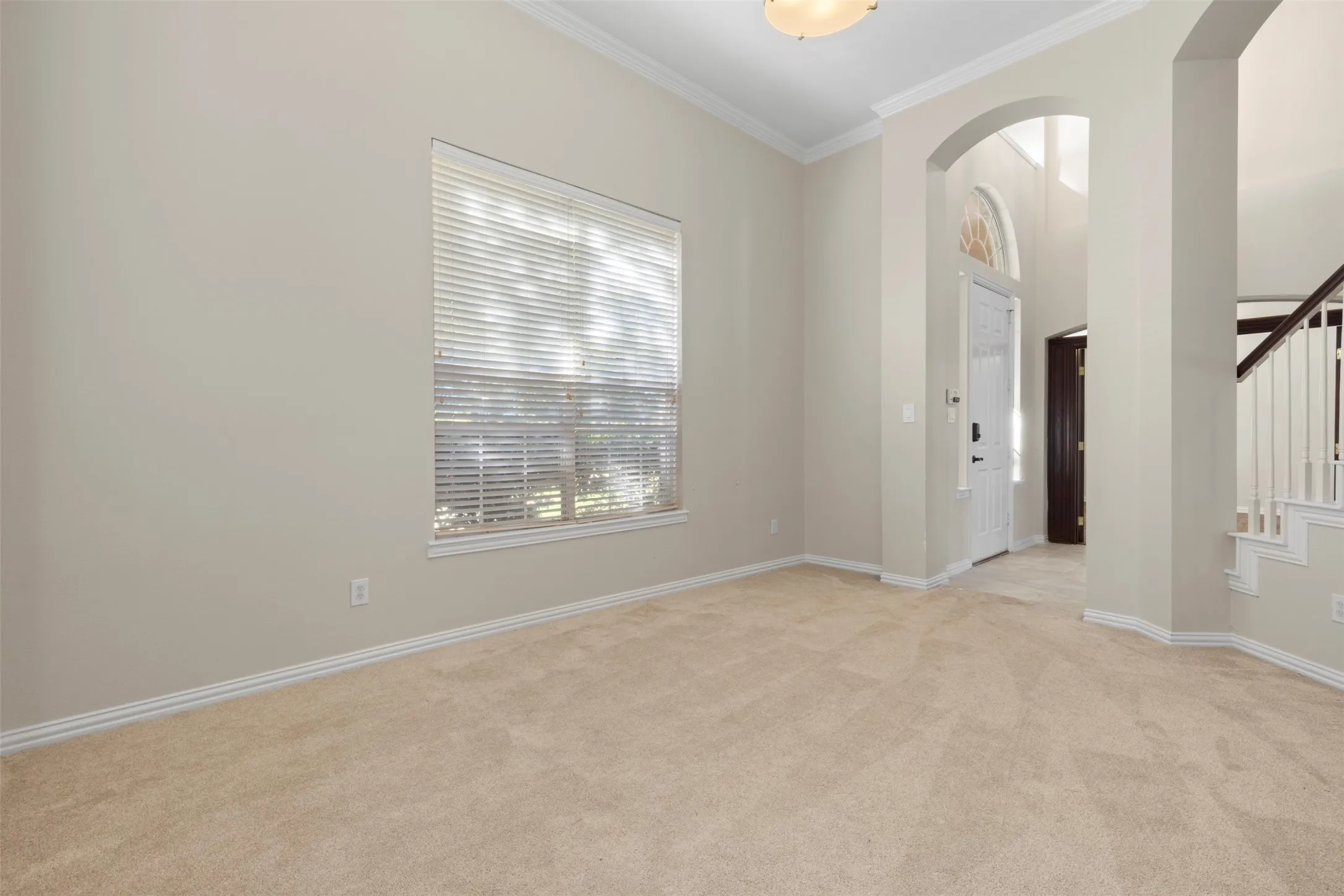 Neutral tone wall paint, crown molding, arched entryways, natural light from a large window, and light-colored carpeting