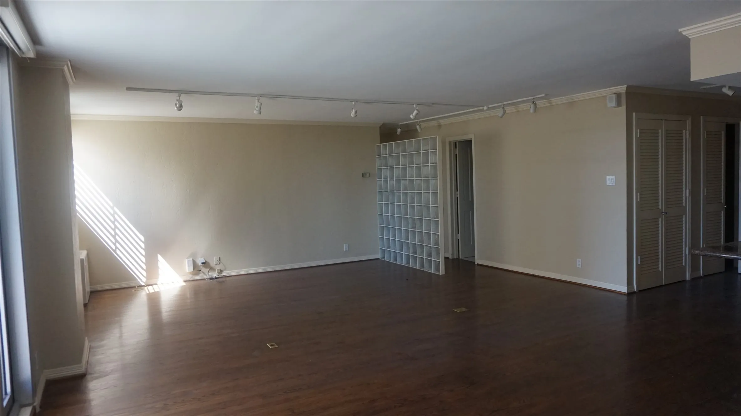 Spacious room featuring wood-finish flooring, track lighting, and glass block partition