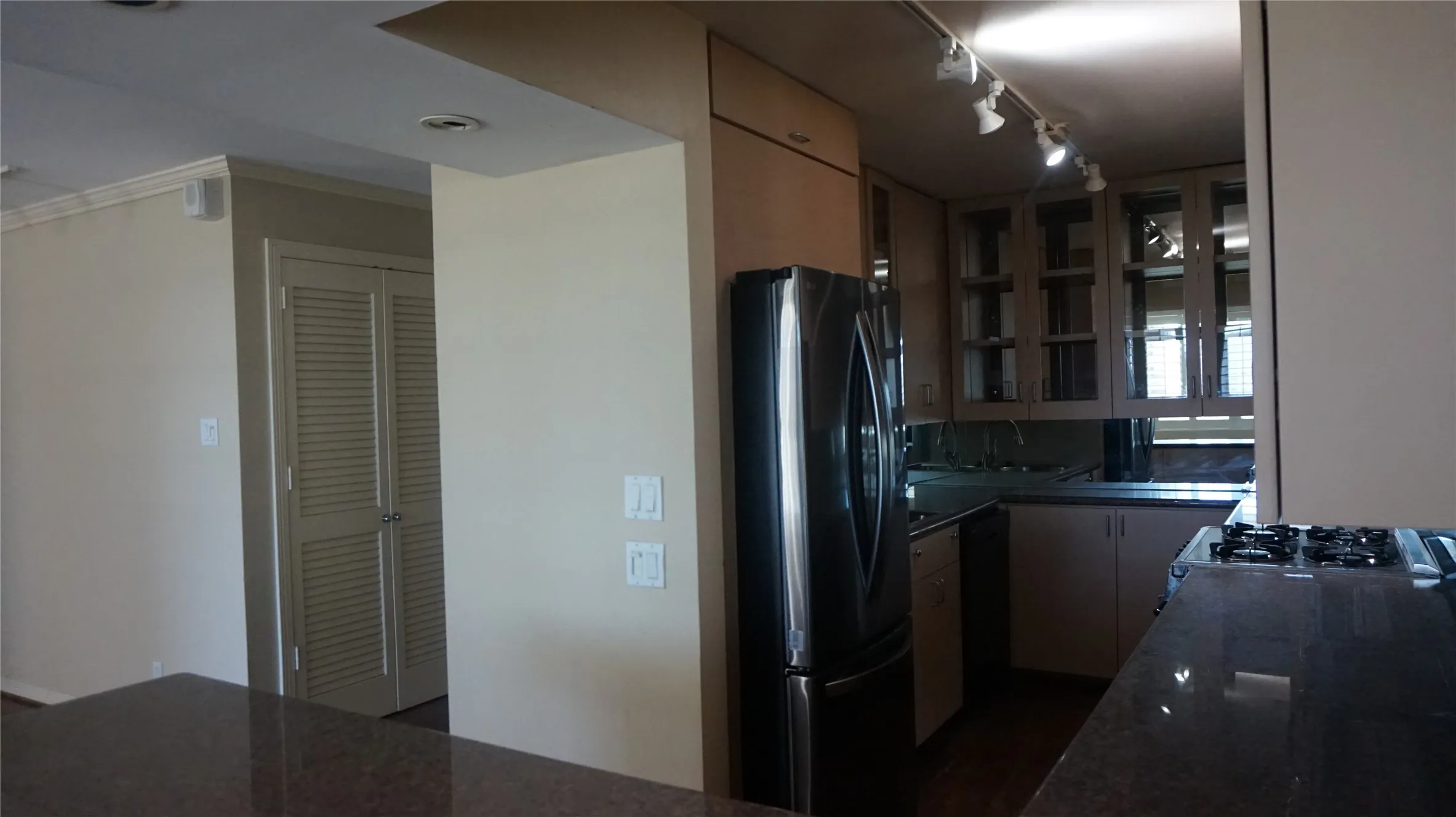Kitchen featuring a stainless steel refrigerator, dark stone countertops, wood-finish cabinetry with glass inserts, and a built-in cooktop