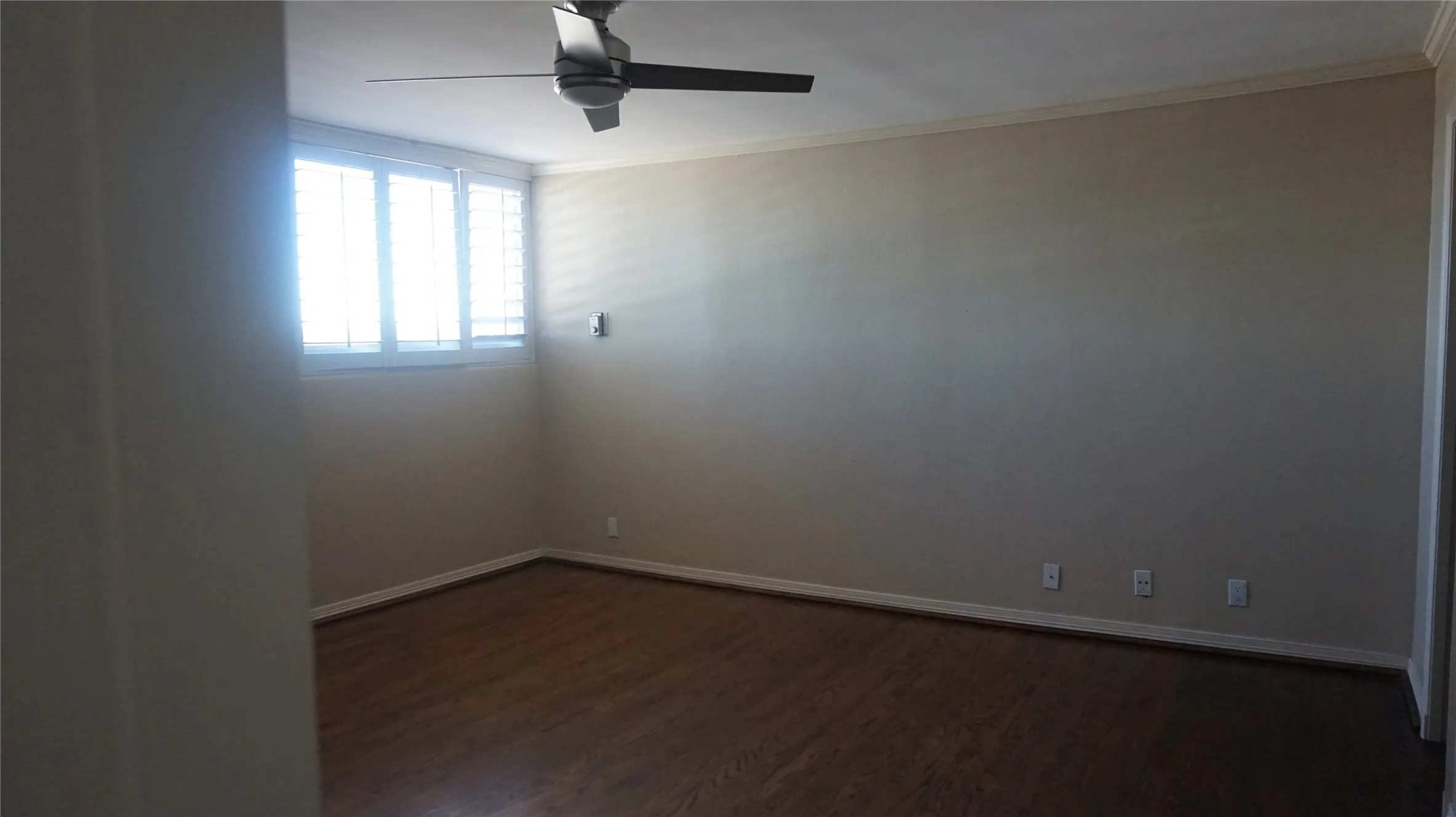 Wood-finish flooring, ceiling fan, crown molding, plantation shutters, and light-toned wall finishes
