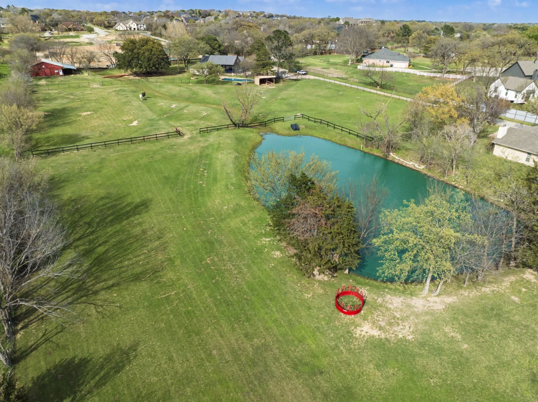 Expansive green property featuring a private pond, perimeter fencing, and mature trees