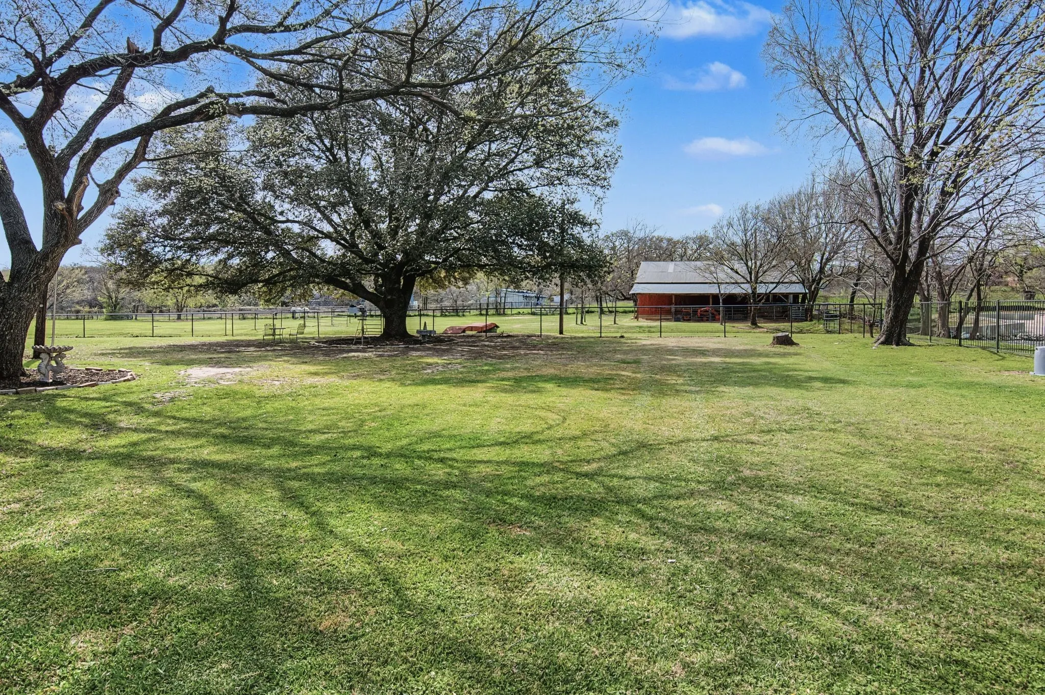 Expansive grassy lawn with mature trees and a fenced perimeter