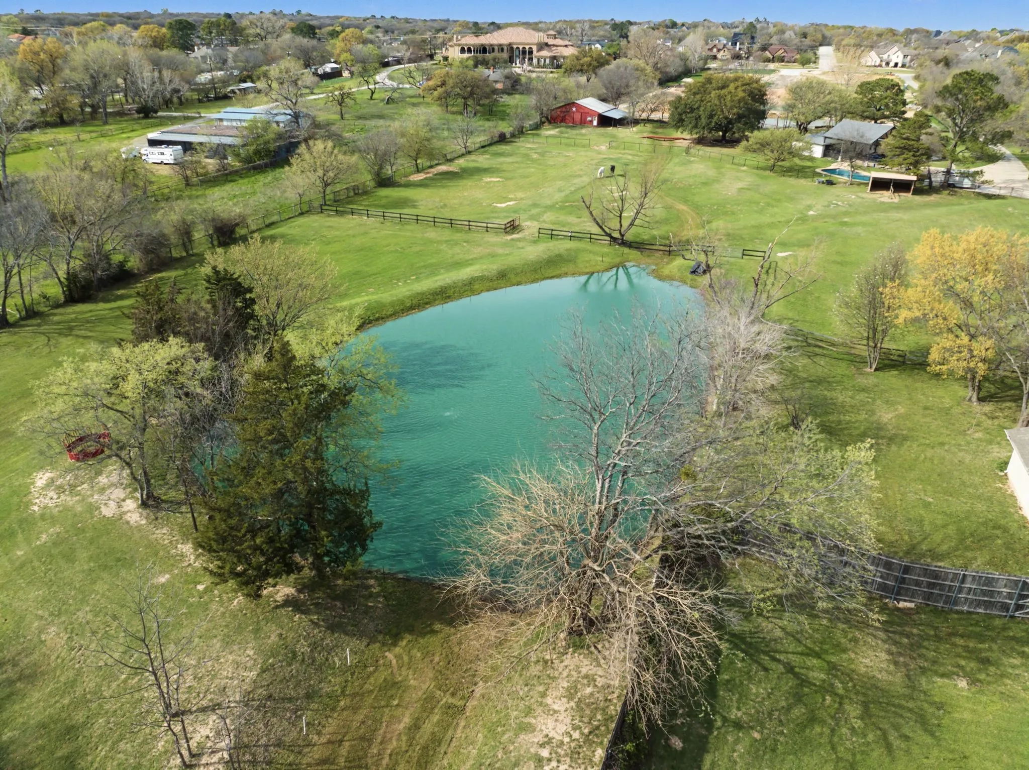 Expansive grounds featuring a pond, established trees, lush green grass, and perimeter fencing