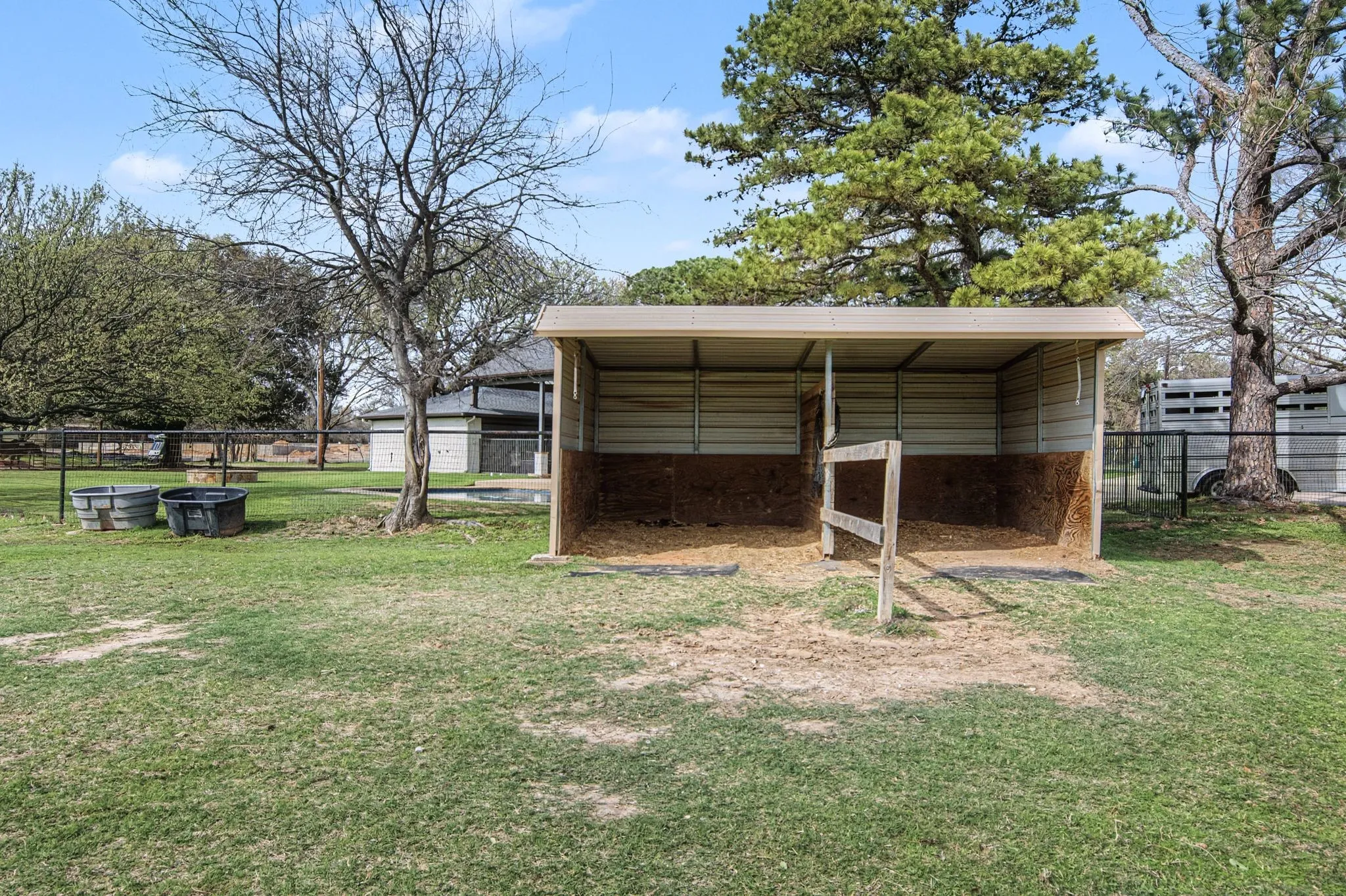 Open-air structure with a metal roof and two stalls, set on a grass expanse